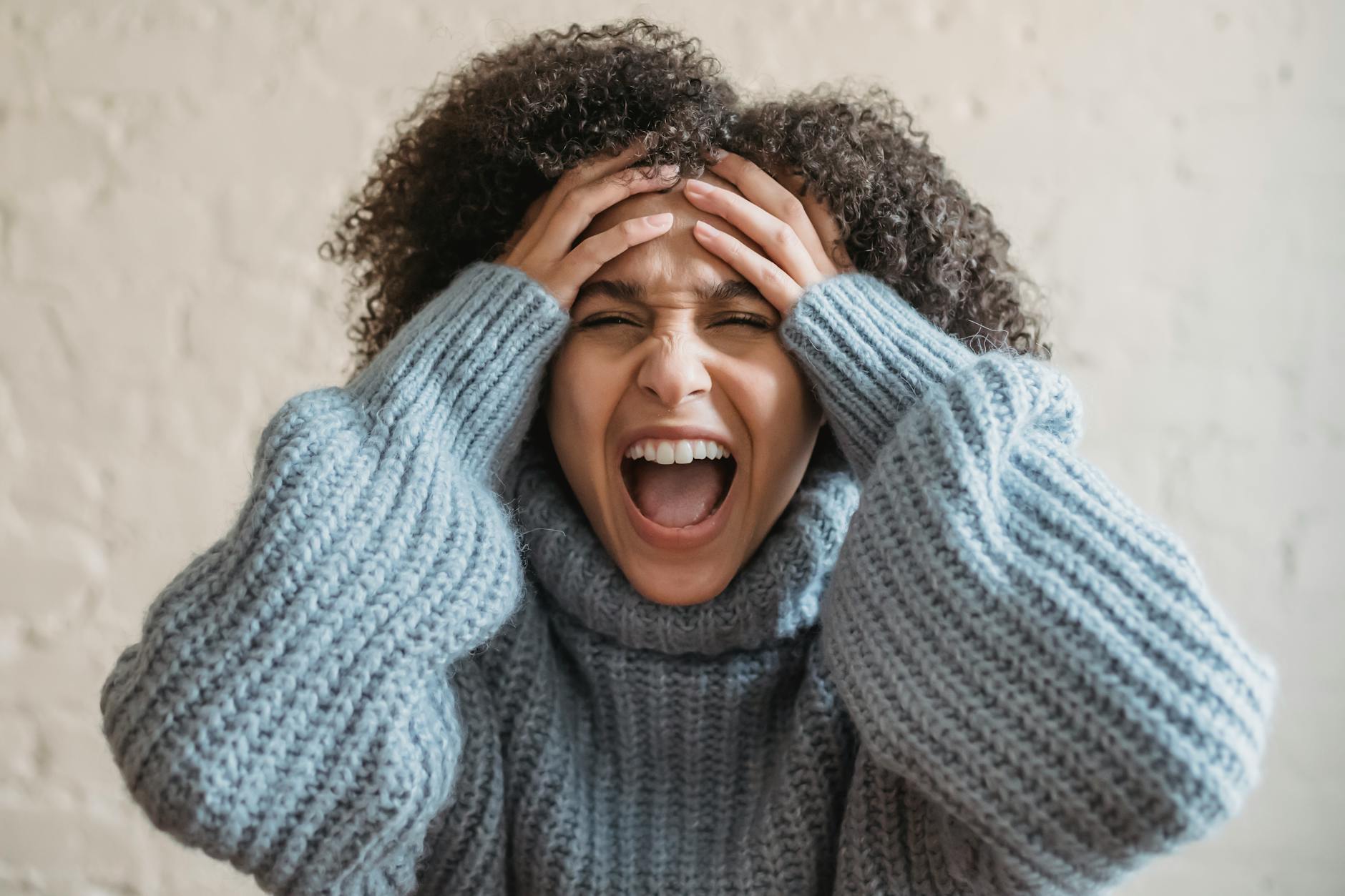 A woman wearing a sweater, expressing frustration with hands on head. - spring anxiety management