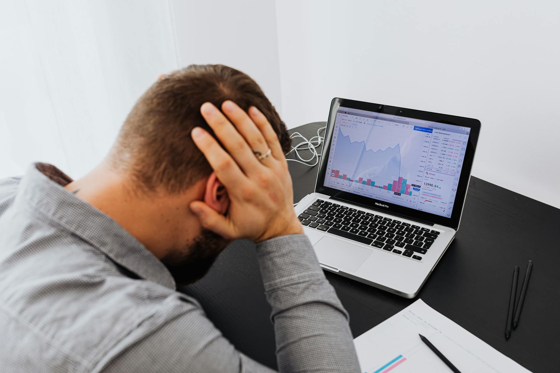 Stressed man at desk looking at declining stock charts on laptop, indicating financial loss. - spring anxiety management