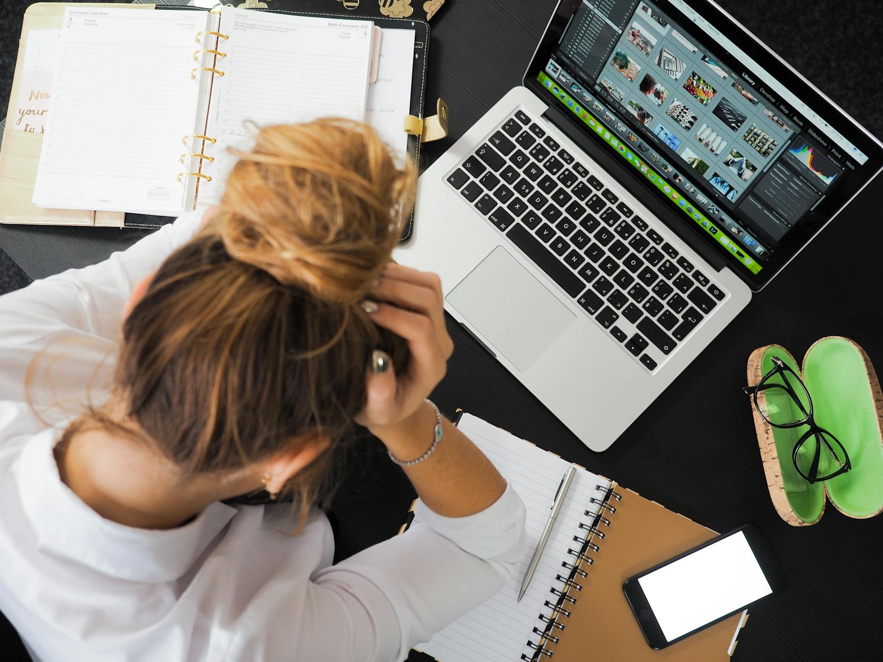 Overhead view of a stressed woman working at a desk with a laptop, phone, and notebooks. - spring anxiety management