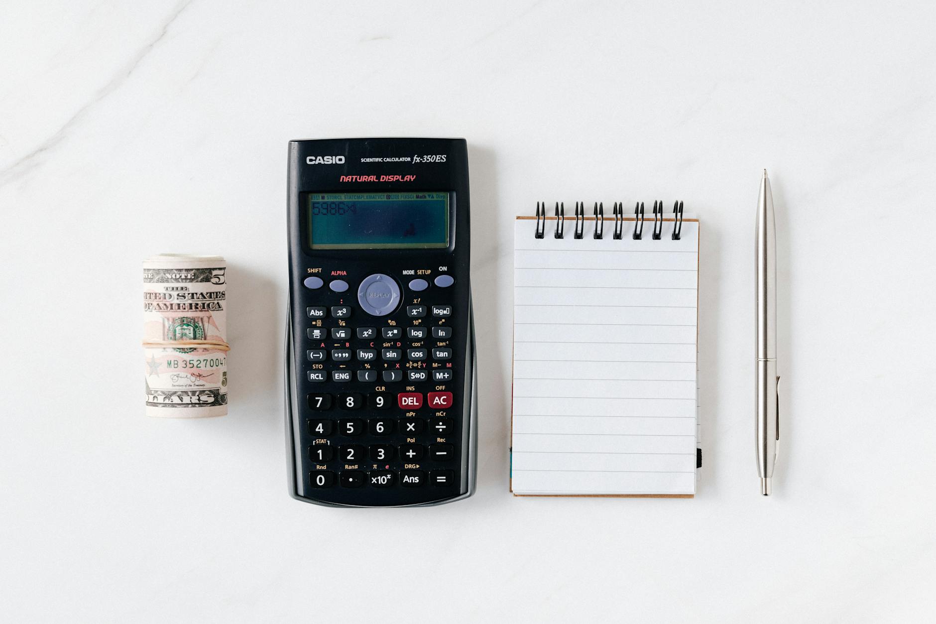Top view of financial tools including a calculator, notepad, pen, and rolled cash on a white background. - spring anxiety management