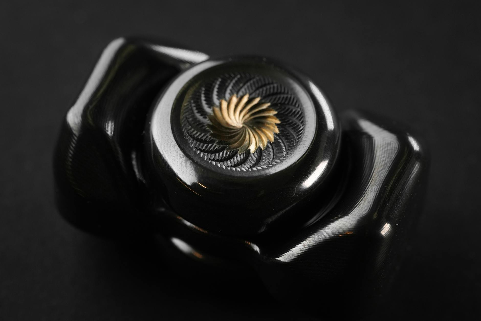 Close-up of a sleek black metal fidget spinner with intricate design against a dark background. - spring anxiety relief