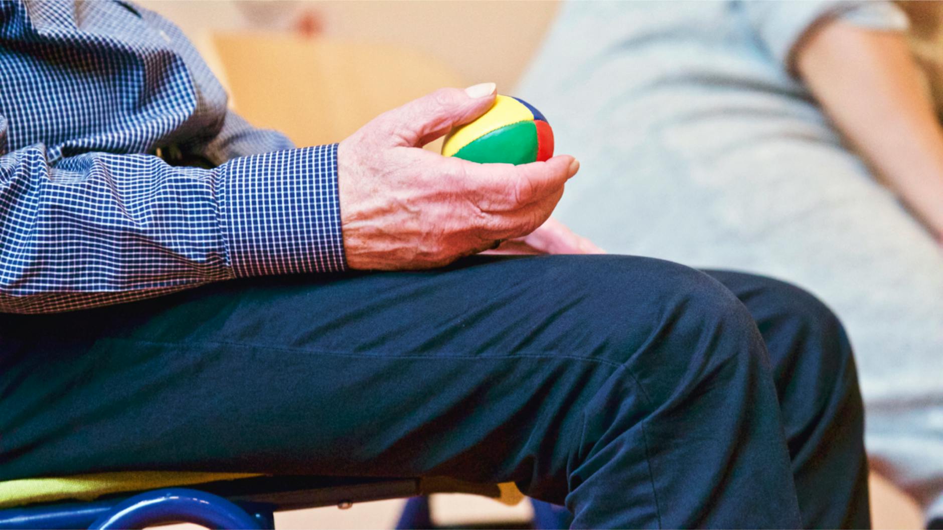 Elderly man holding a colorful therapy ball indoors, promoting relaxation and health. - spring blues therapy