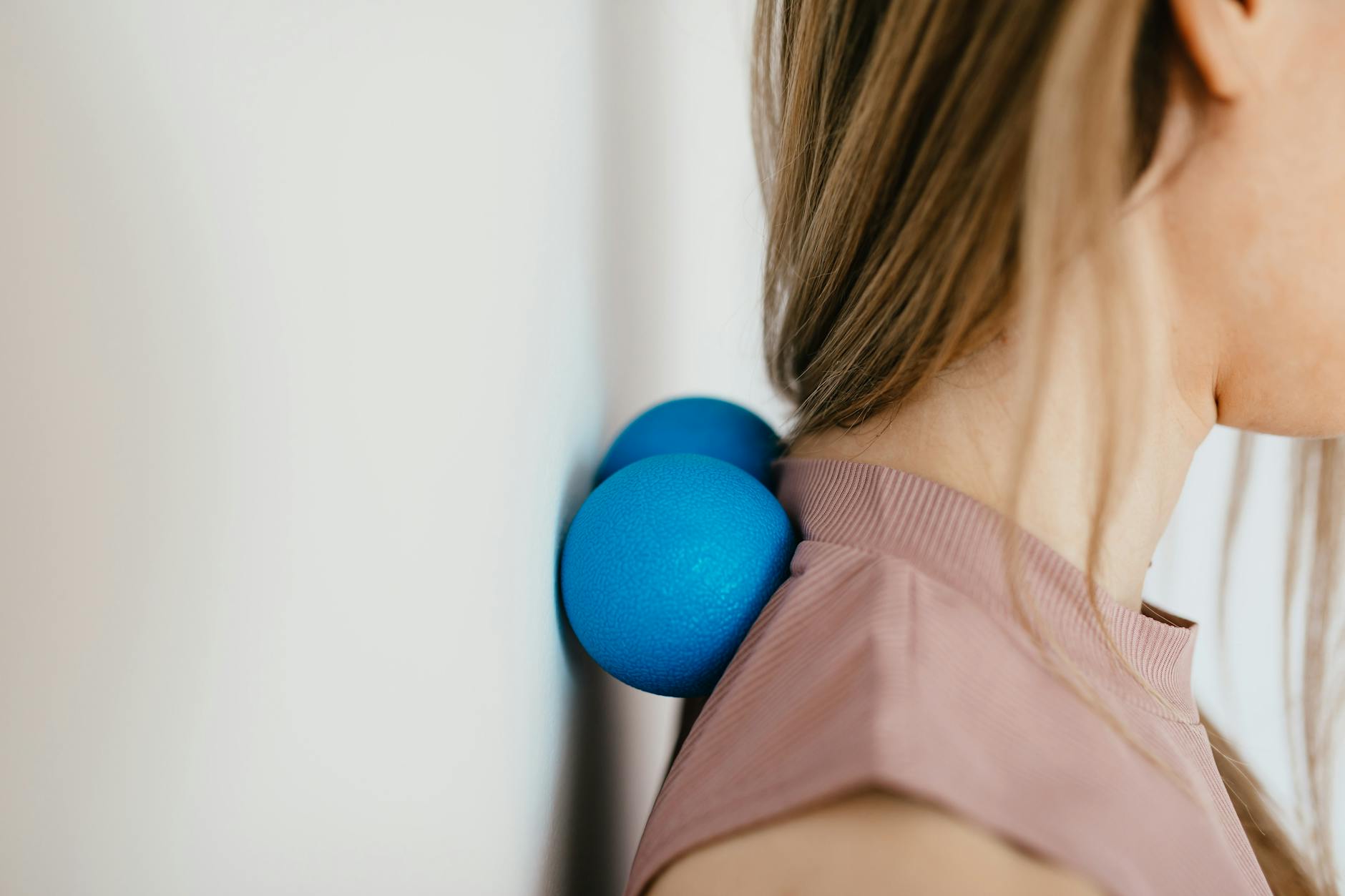 Close-up of woman using blue massage balls for neck relief against a wall. - spring blues therapy