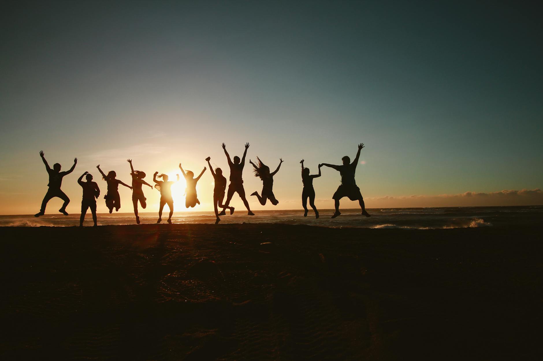 Silhouette of a group of friends jumping on a beach at sunset, expressing joy and freedom. - spring break activities