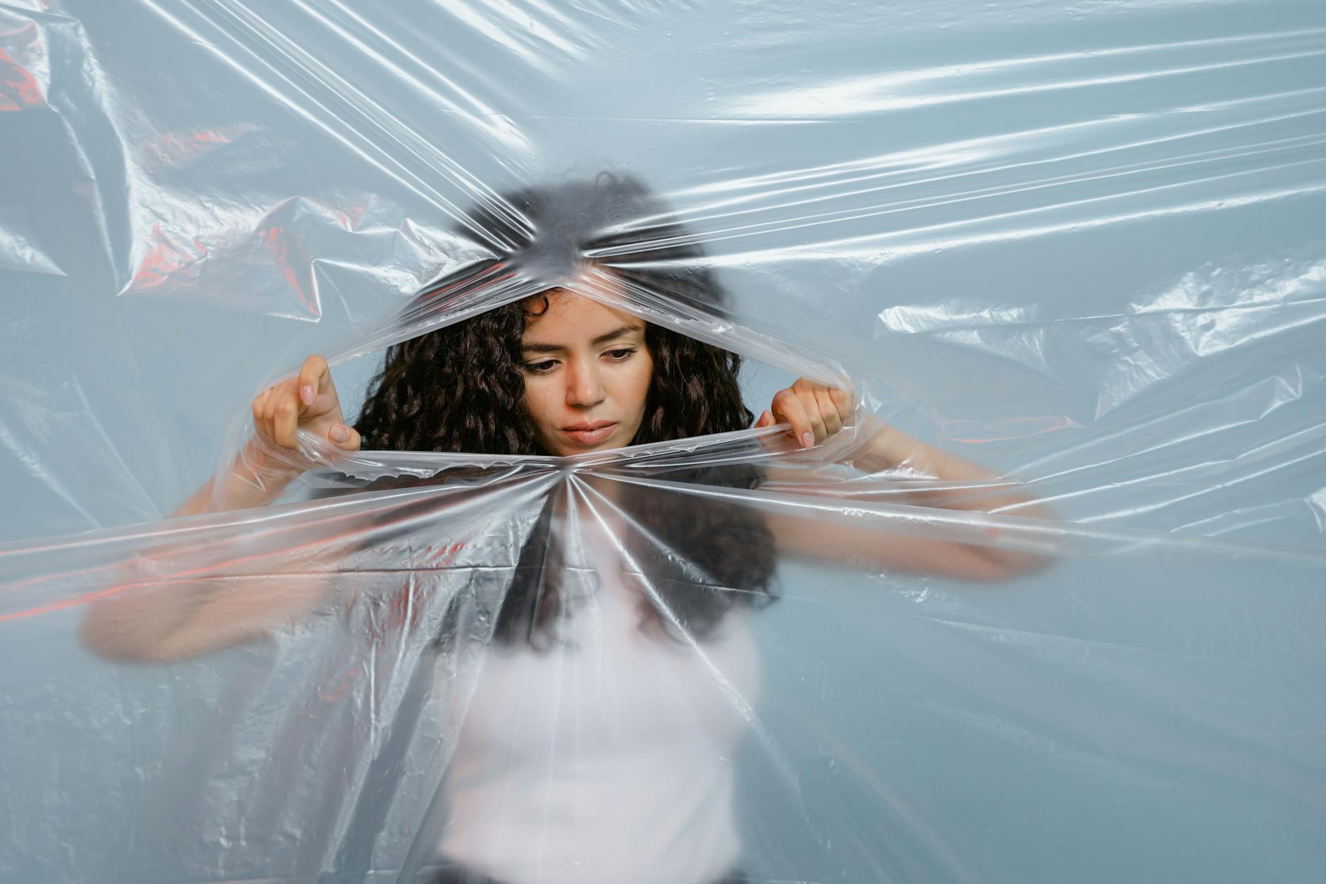 A woman tears a plastic sheet against a blue background, symbolizing breakthrough. - spring break family boundaries