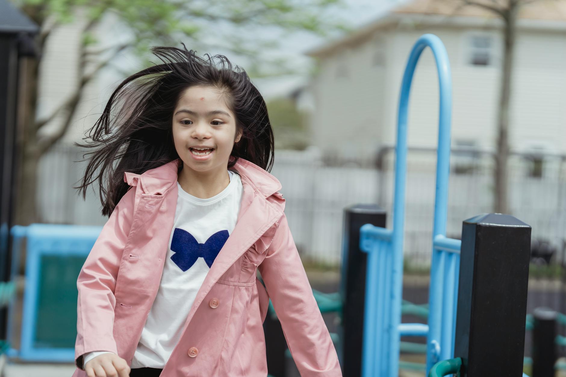 A happy young girl wearing a pink jacket enjoying her time at an outdoor playground on a bright spring day. - spring child energy