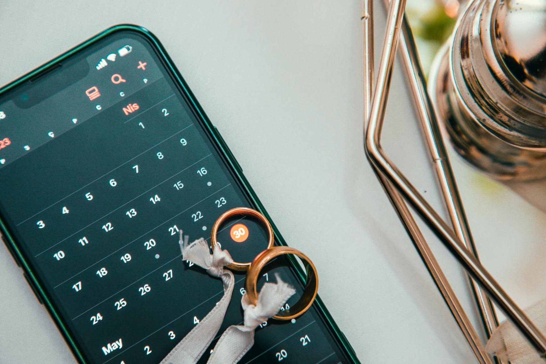 Elegant setup of wedding rings on a smartphone displaying a calendar date, symbolizing planning and celebration. - spring dating app