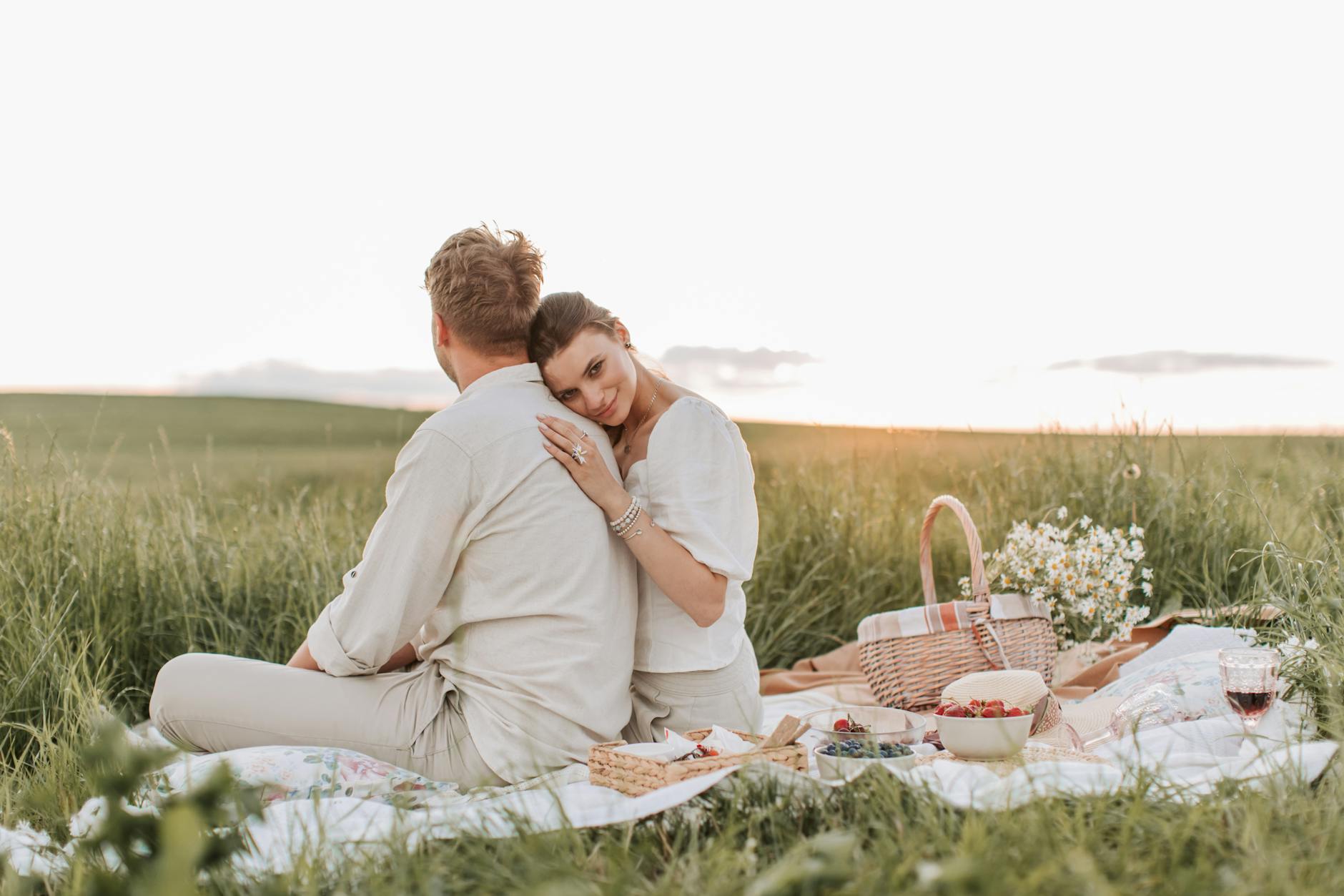 A couple embraces during a sunset picnic, showcasing love and togetherness in a serene field. - spring dating refresh
