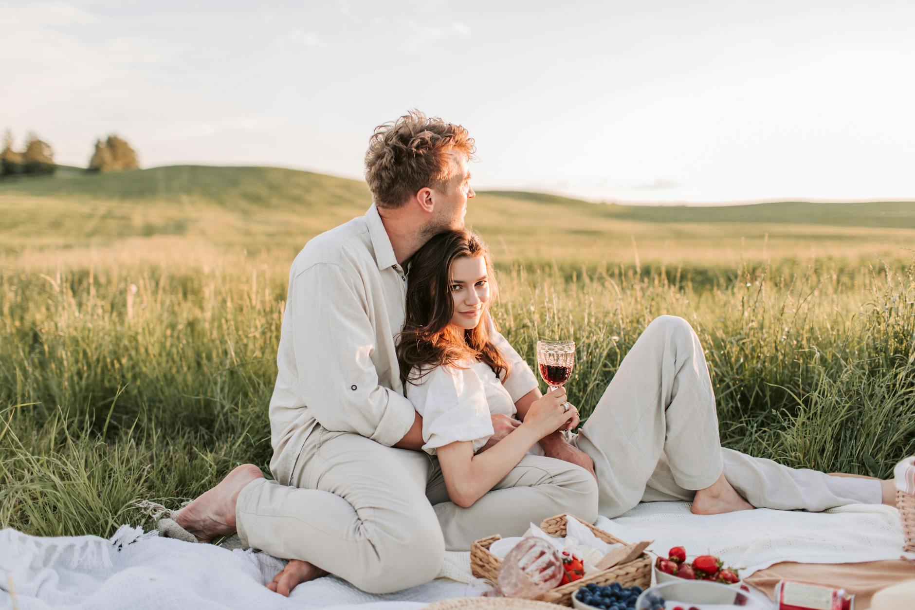 Couple enjoying a romantic picnic in a sunny meadow with wine and snacks. - spring dating refresh