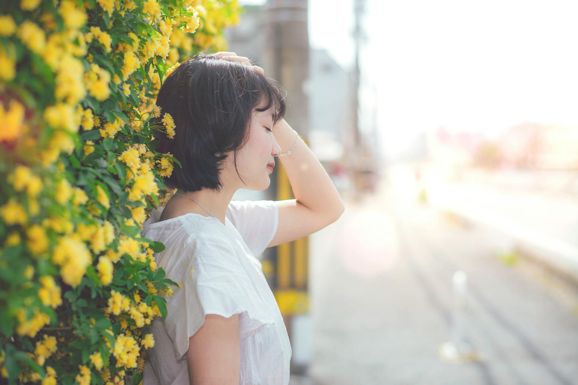 A serene woman enjoying a peaceful moment by a vibrant yellow flowering hedge outdoors. - spring depression symptoms