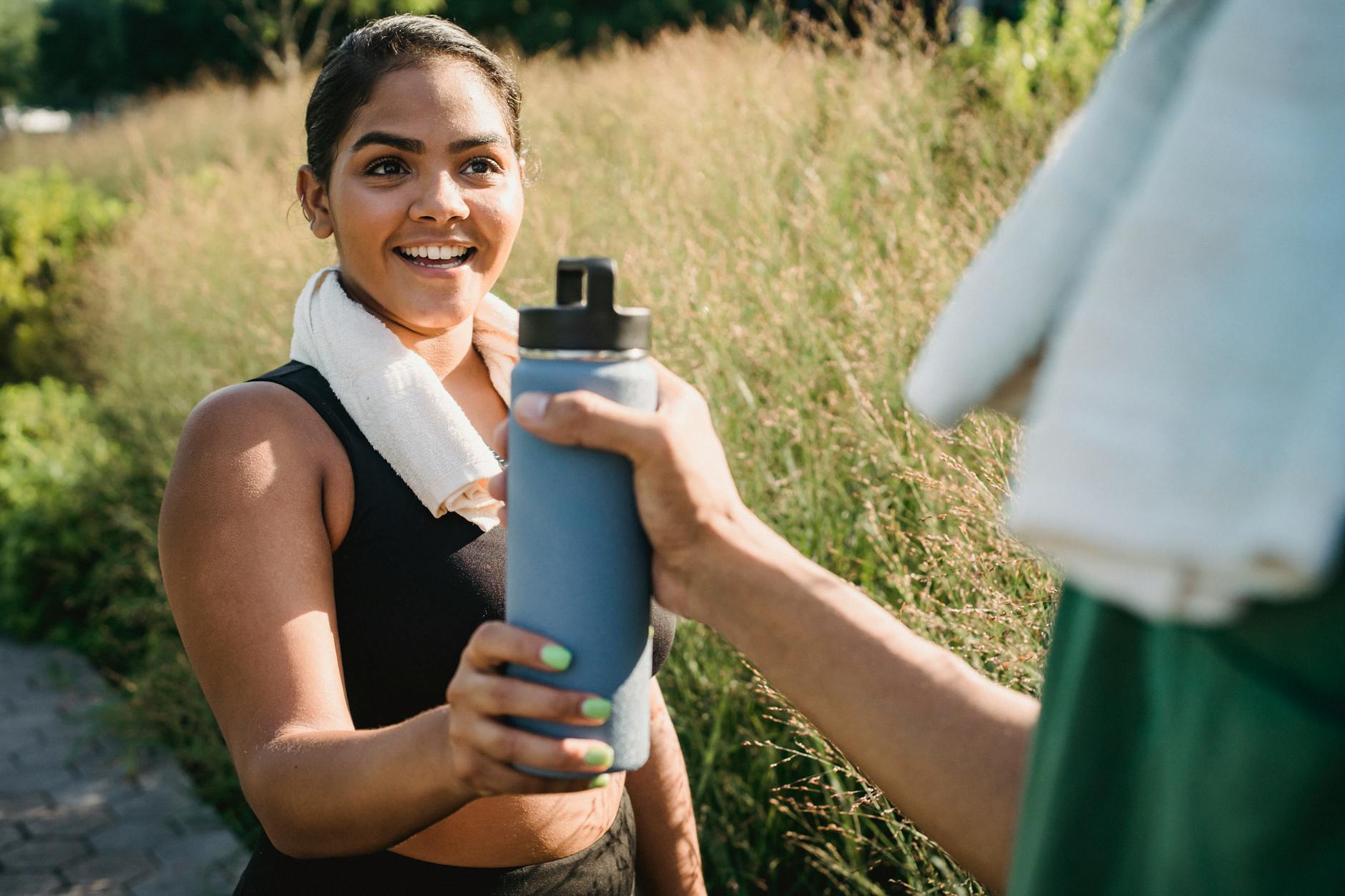 Smiling woman receiving water bottle during outdoor exercise. - spring energy boost