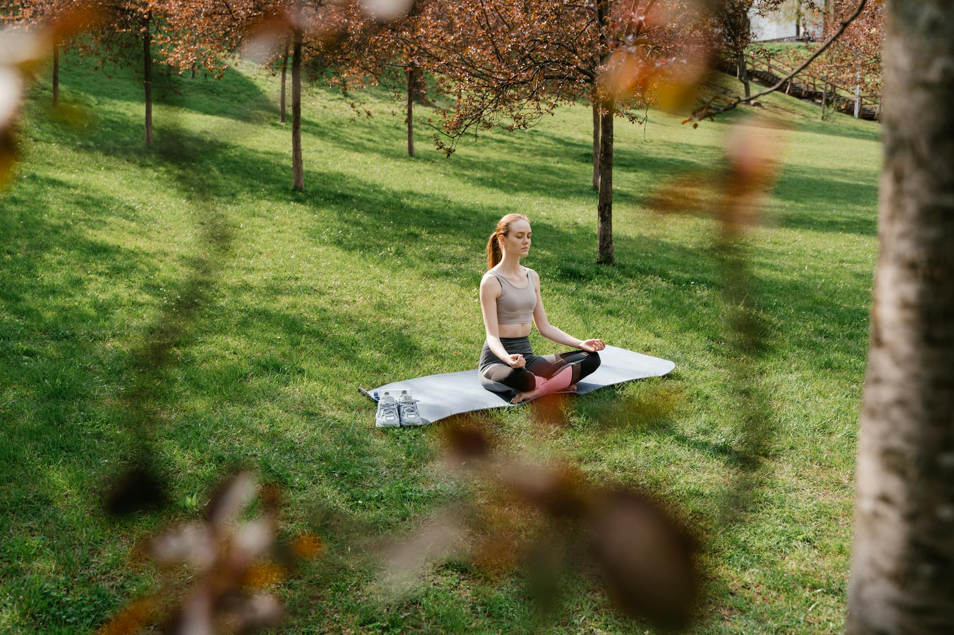A woman meditating on a yoga mat in a sunny park surrounded by trees. - spring mental clarity