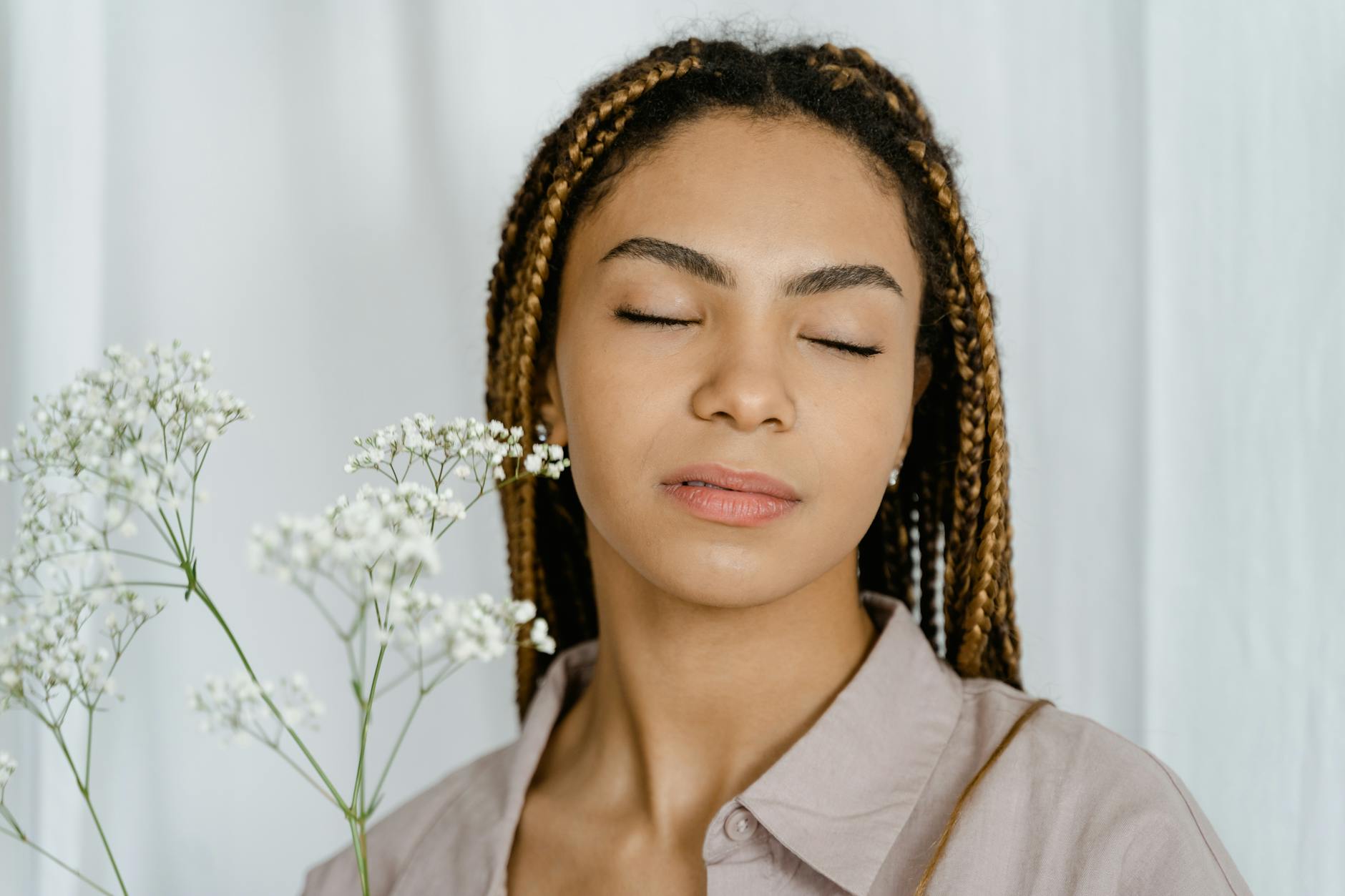Close-up portrait of a serene woman with braided hair, eyes closed, holding white flowers. - spring mood boost