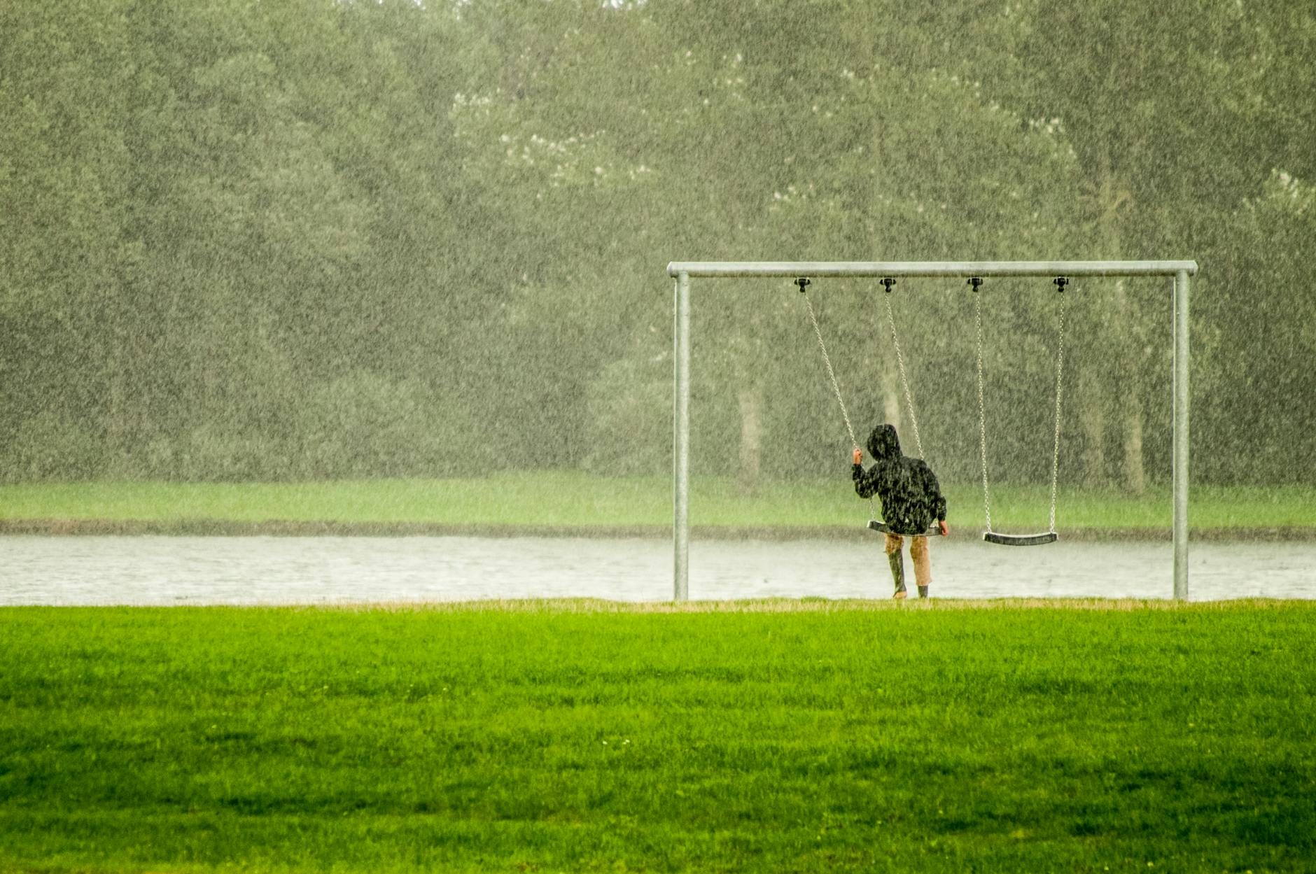 A child on a swing in a rainy park, capturing a serene moment with falling rain. - spring mood swings