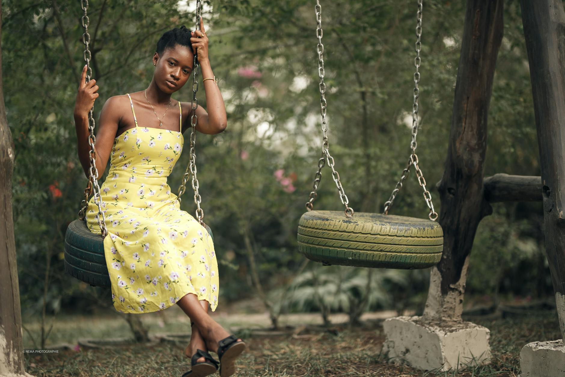 A woman in a yellow floral dress poses on a tire swing outdoors. - spring mood swings