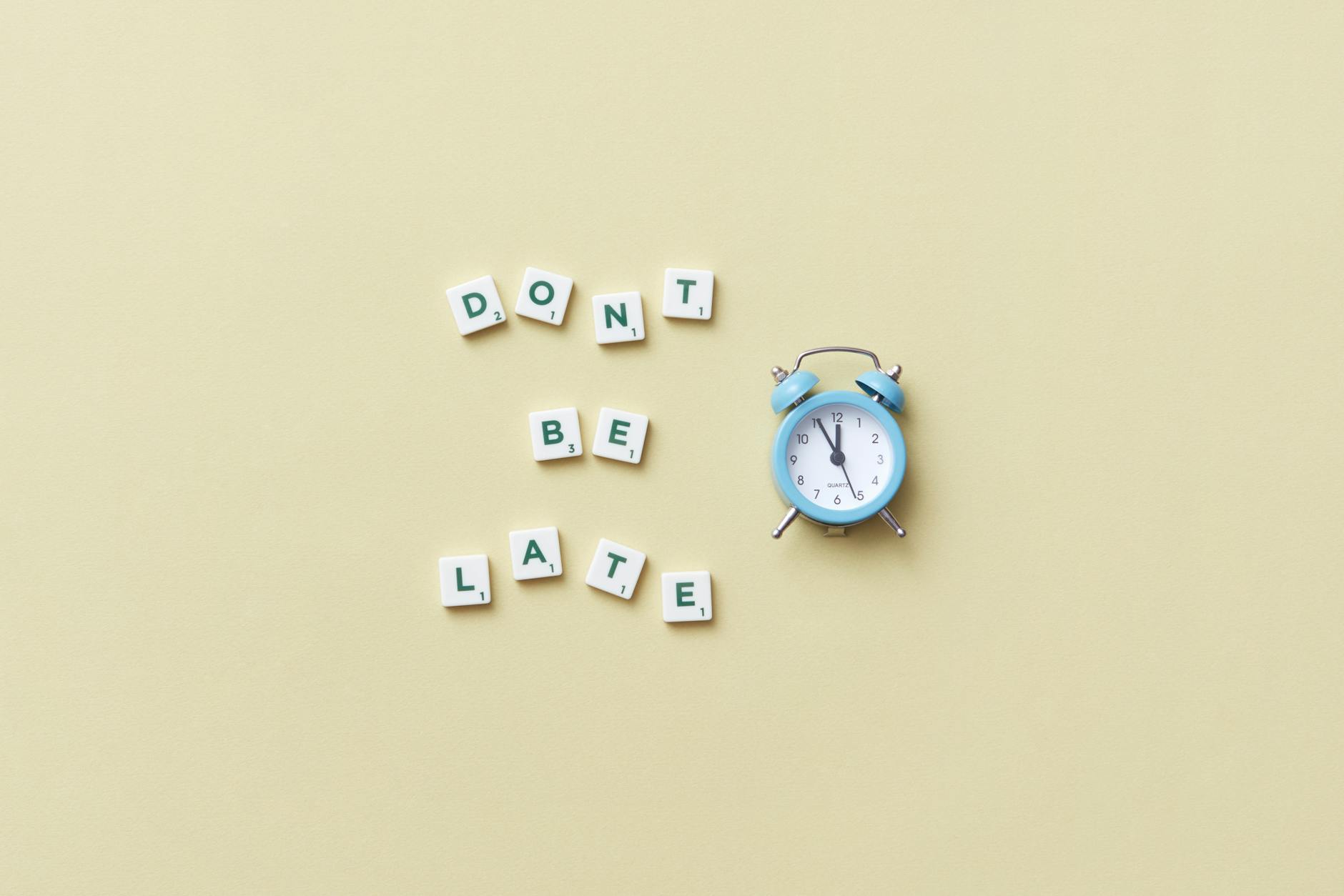 Flat lay of a blue alarm clock and letter tiles spelling 'Don't Be Late'. - spring procrastination therapy