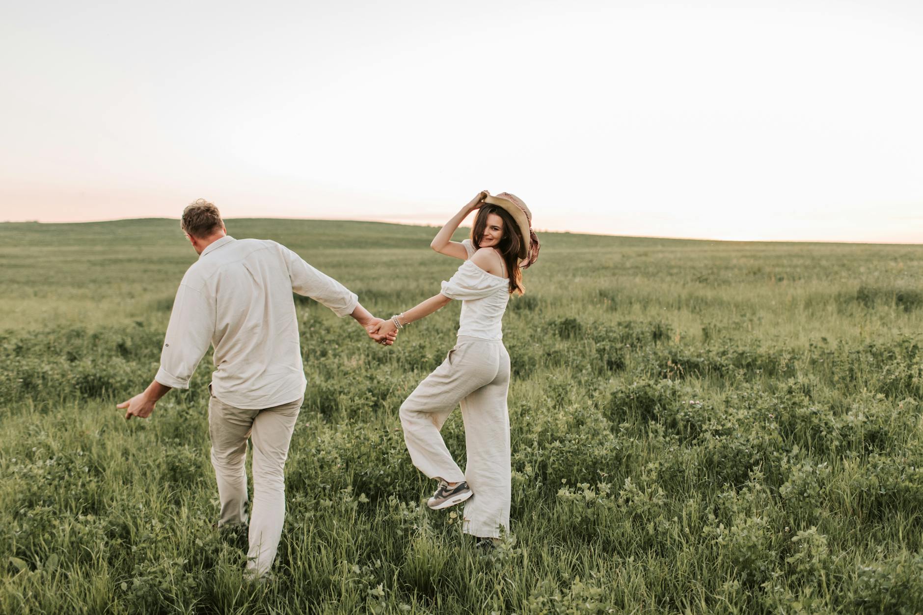 A happy couple strolling hand in hand through a green field on a sunny day. - spring relationship reconnection