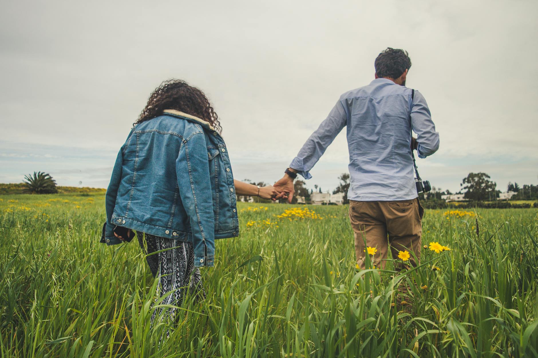 Couple holding hands walking through a green field with yellow flowers, embodying connection and nature. - spring relationship reset
