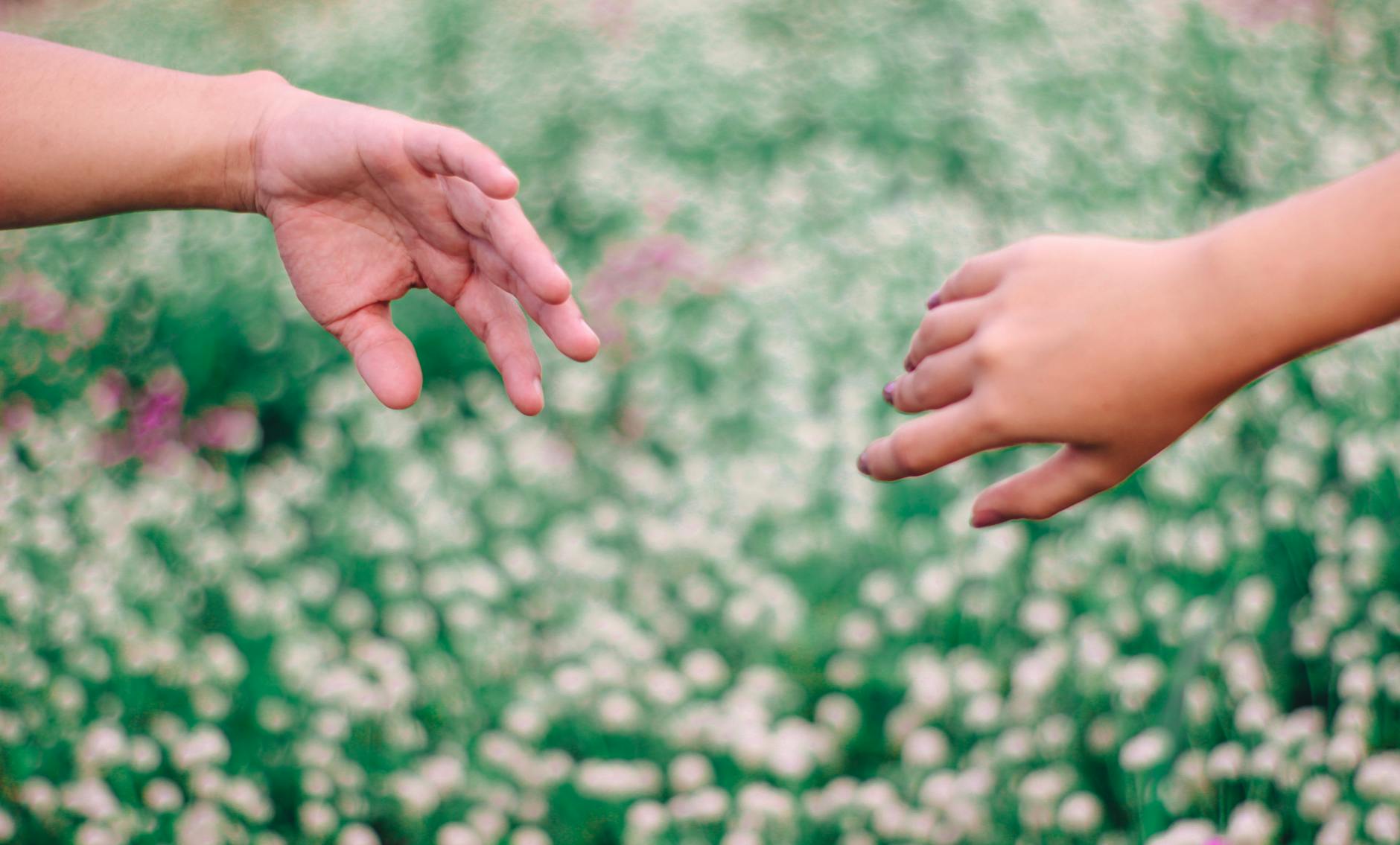 Two hands reaching towards each other against a blurred floral background, symbolizing connection. - spring relationship reset