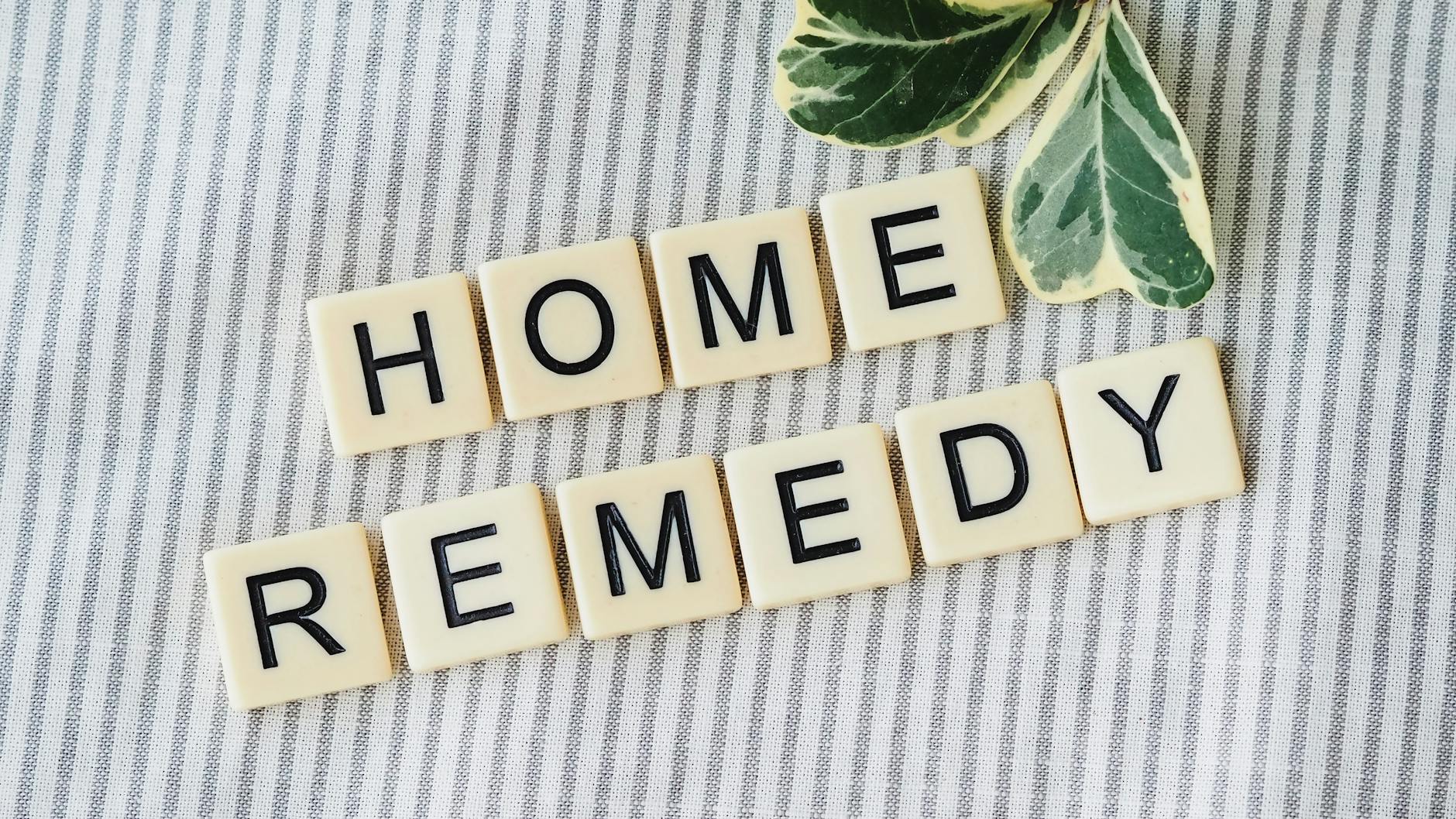 Scrabble tiles forming 'Home Remedy' with green leaves on a striped background. - spring slump remedies