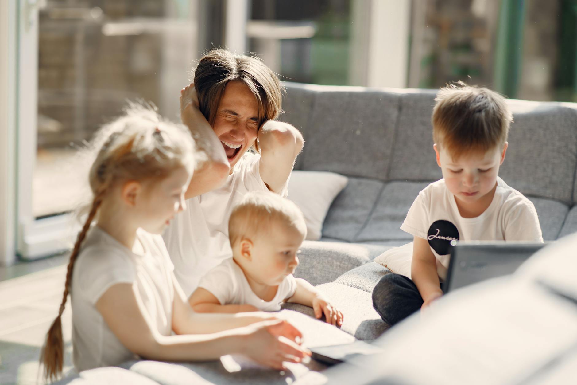 Woman going mad while sitting with little kids playing together on sofa in well lit room - spring social anxiety