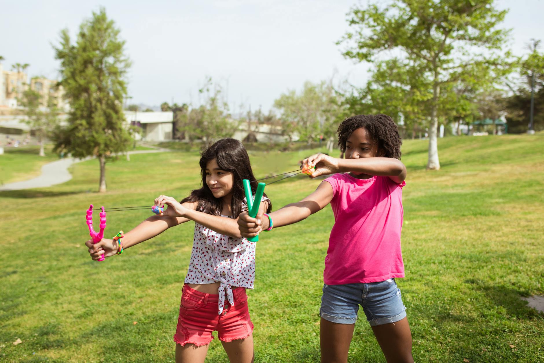 Two girls having fun in a park with toy slingshots on a sunny day. - summer camp transition