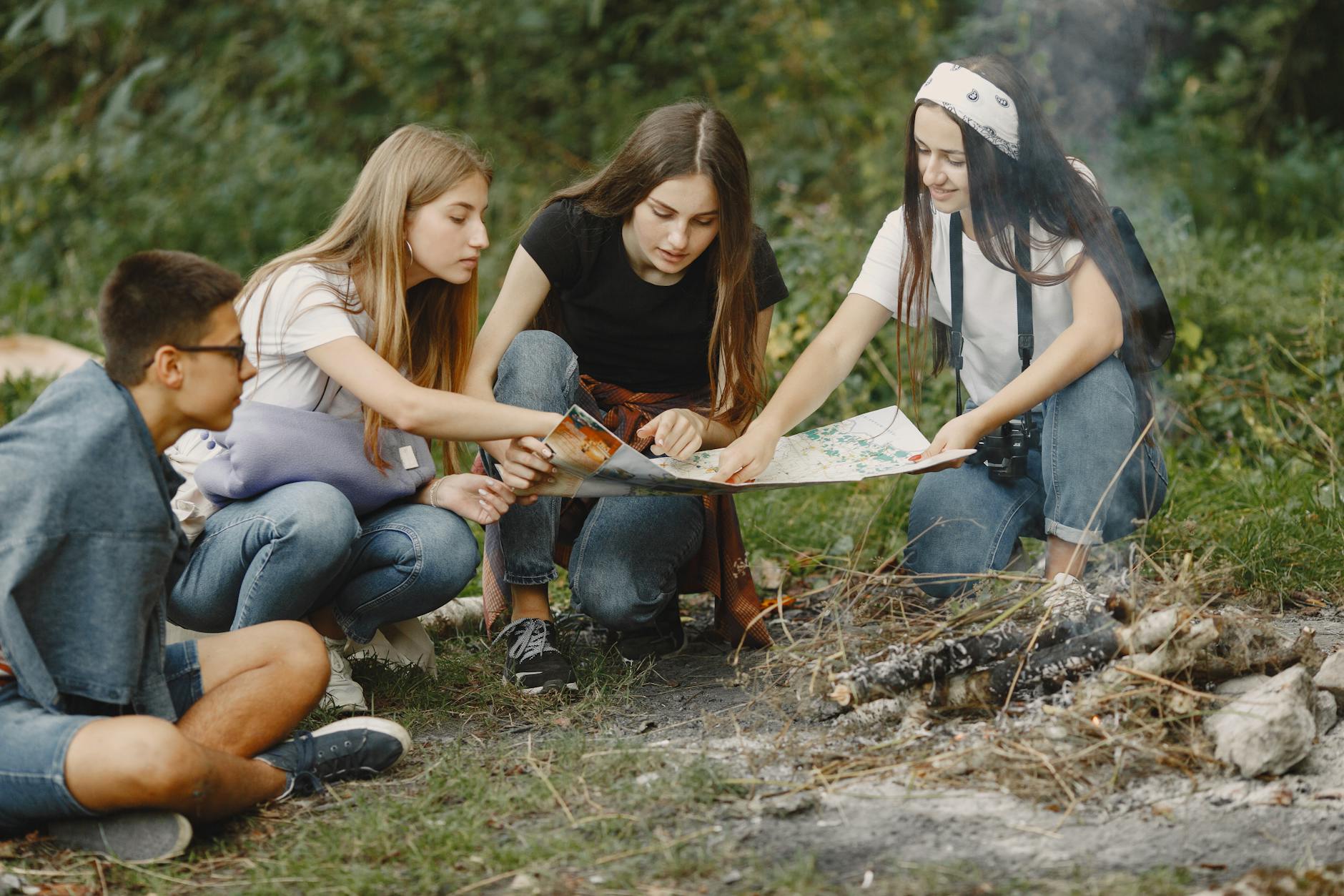 Group of teens sitting around a campfire, planning adventure with a map. - teen summer plans