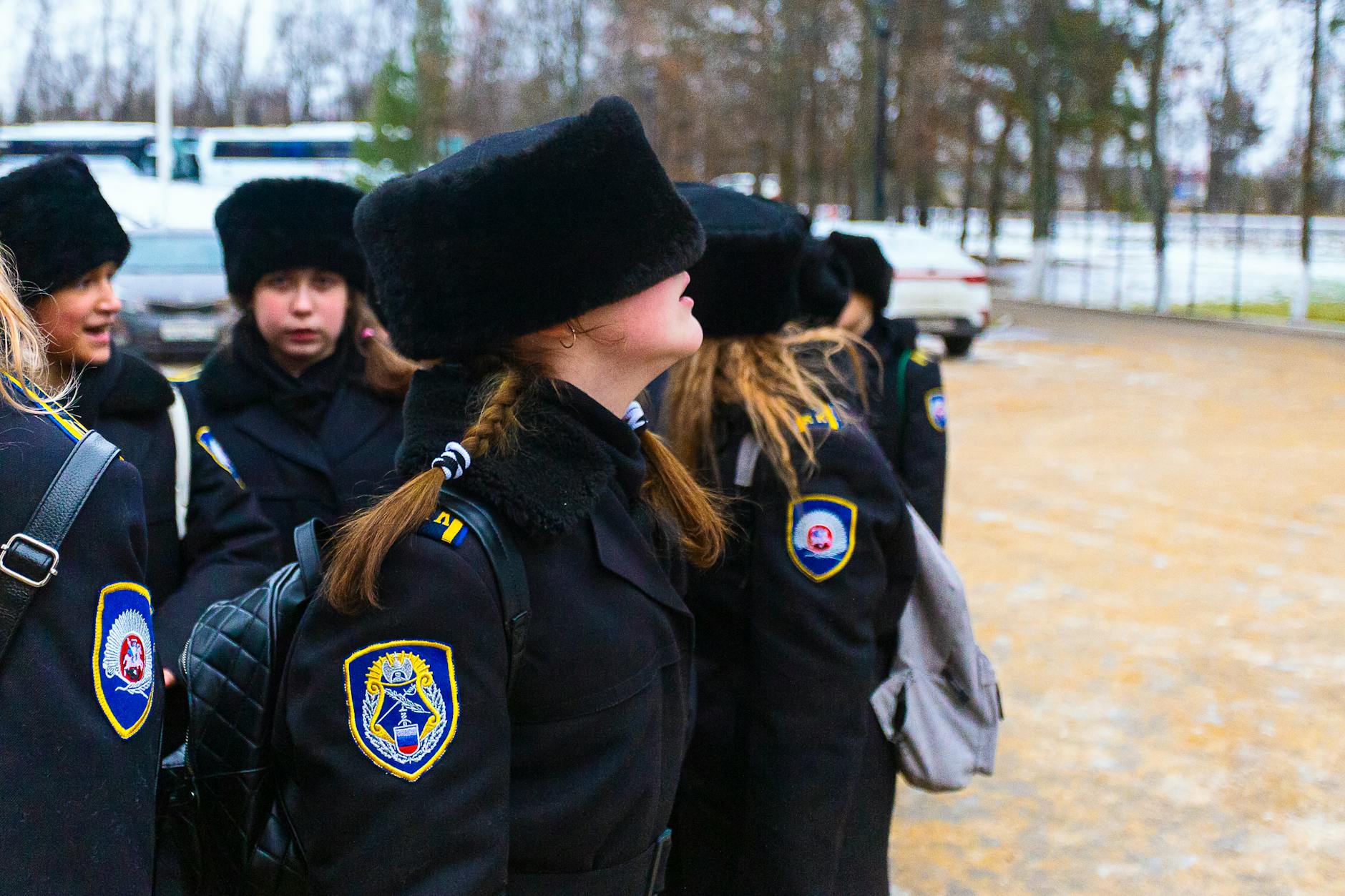 Schoolgirls in matching uniforms and fur hats stand outdoors in a winter setting, displaying lively camaraderie. - teen winter blues