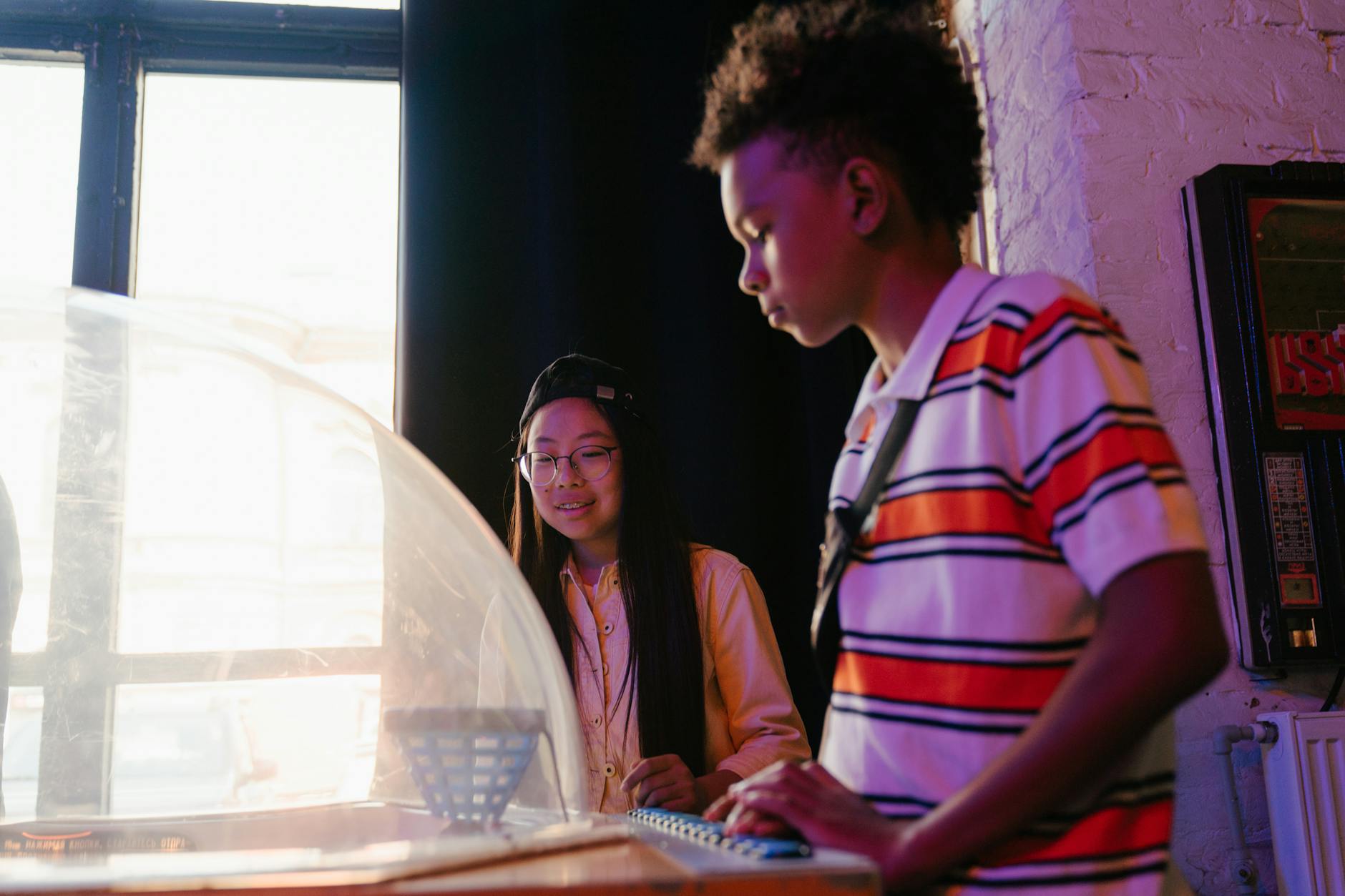 Two teenagers playing an arcade game indoors, enjoying a retro ambiance in sunlight. - teen winter blues