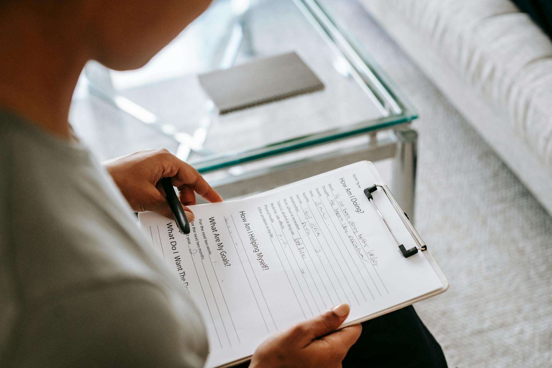 From above of blurred anonymous female psychologist reading documents on clipboard while sitting in office near table during session - therapeutic journaling prompts