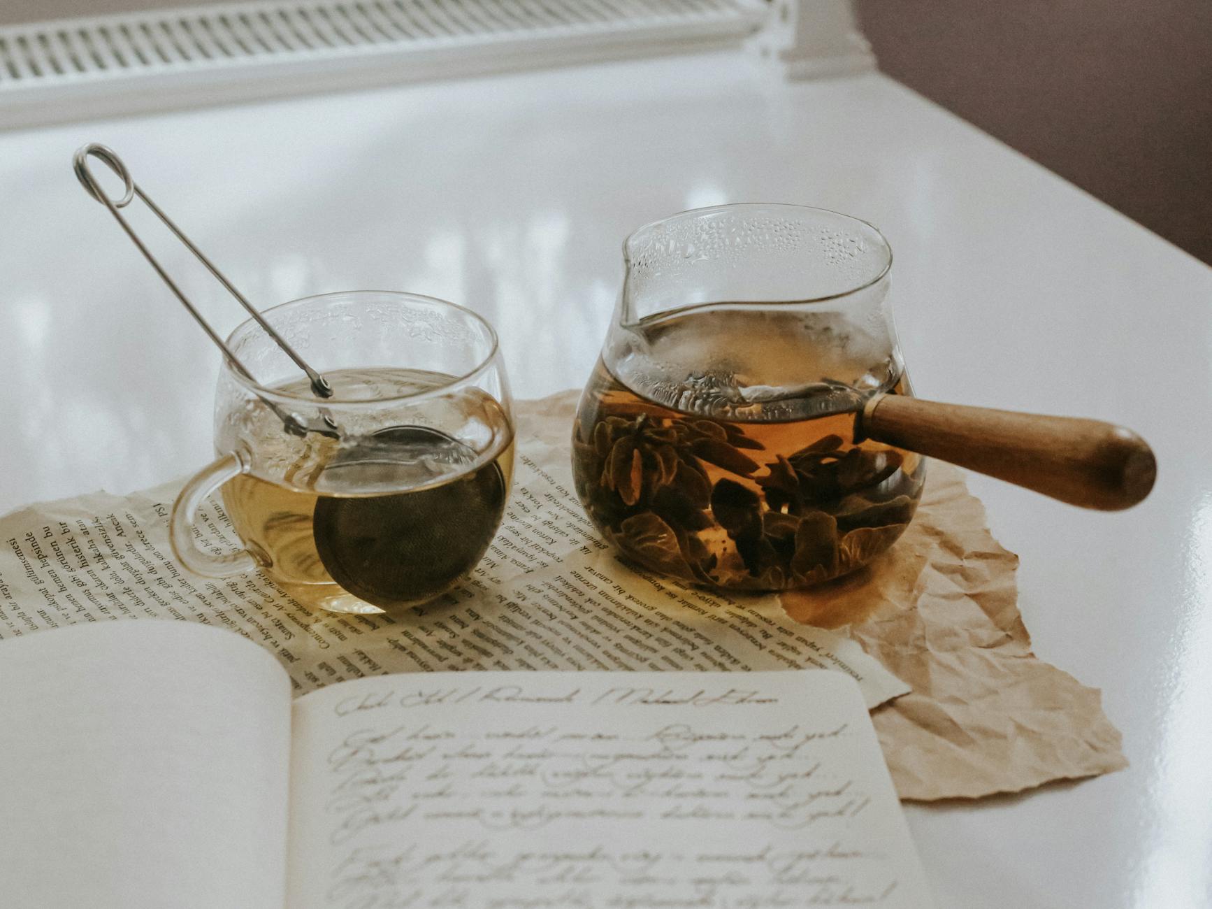 A warm tea scene with a glass cup, teapot, and open journal, evoking cozy indoor vibes. - therapeutic journaling prompts