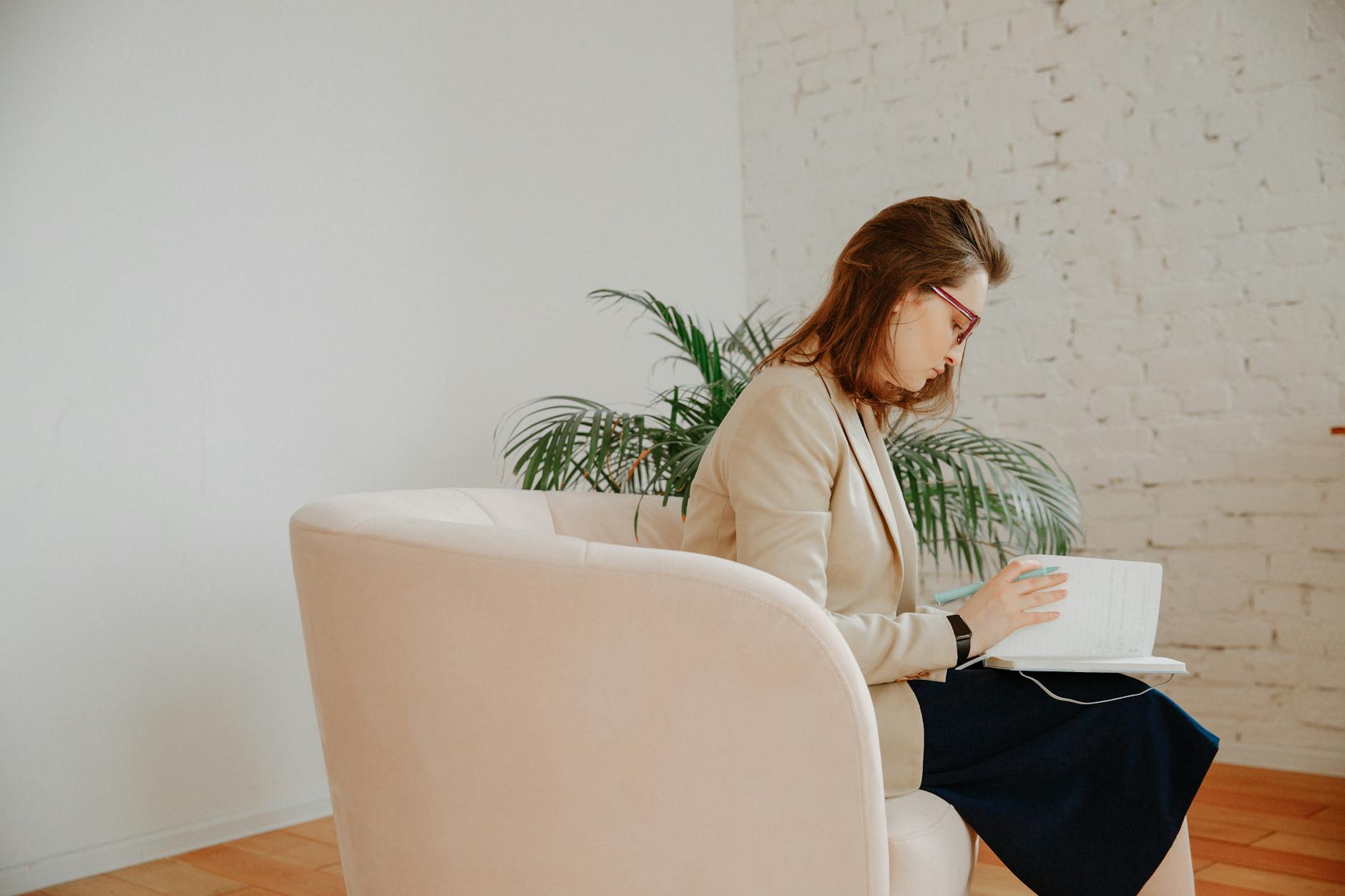 Female therapist writing notes during a session in a serene, neutral-toned office. - therapeutic journaling prompts