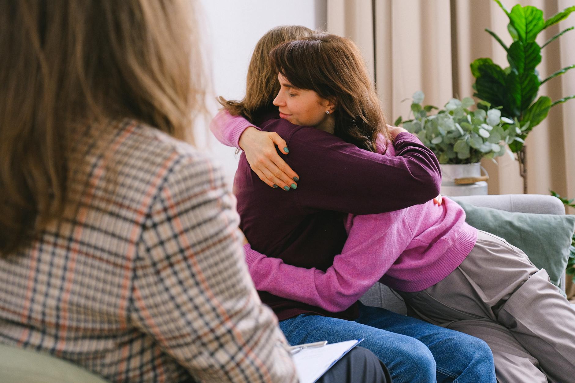 Side view of couple sitting on sofa and embracing during session with psychologist in light room in daytime - therapist for seasonal mood shifts