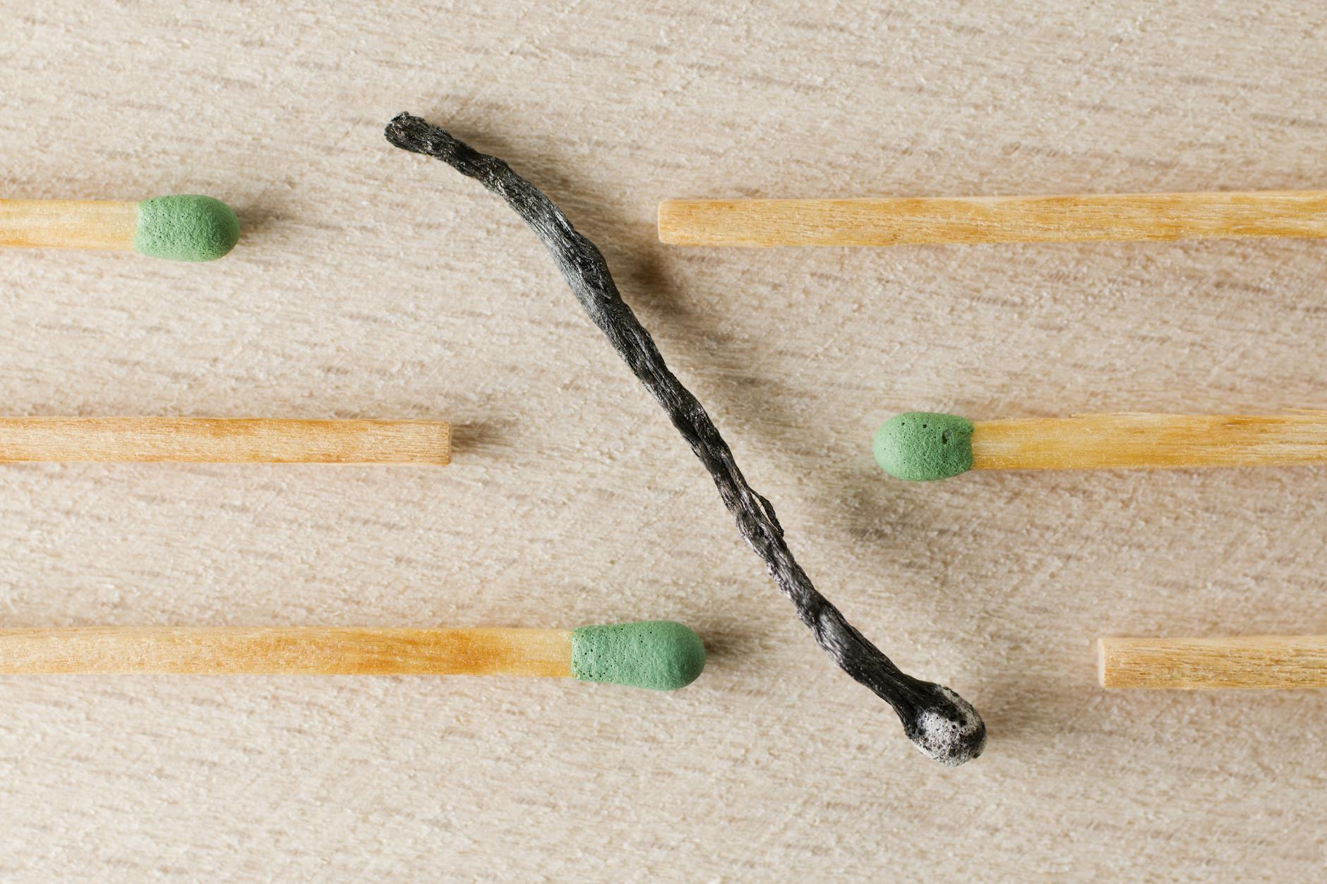 Charred match surrounded by green-tipped matches symbolizing burnout and contrast. - therapy for burnout