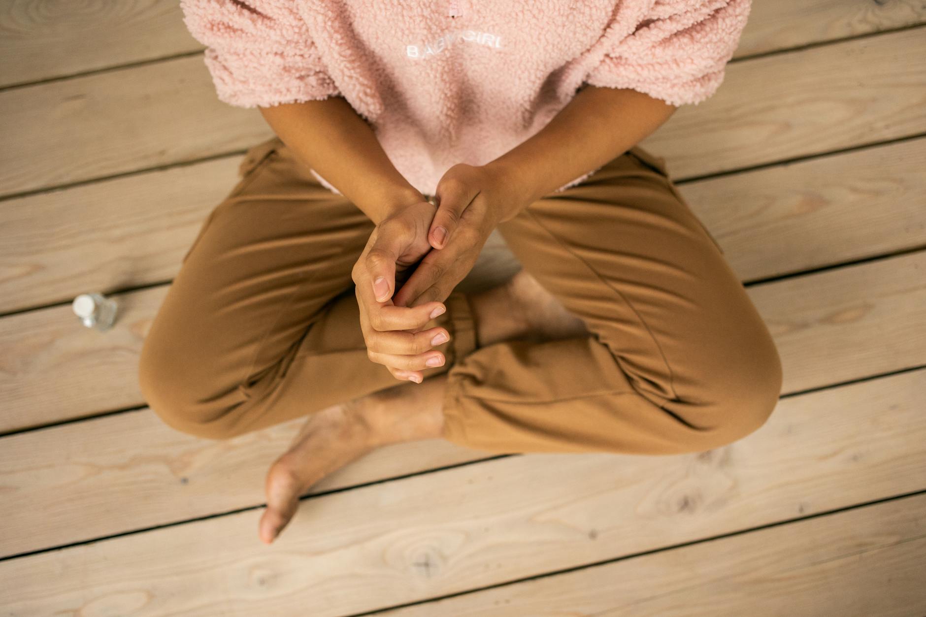 Woman sitting cross-legged indoors, practicing self care on a wooden floor. - therapy intentions