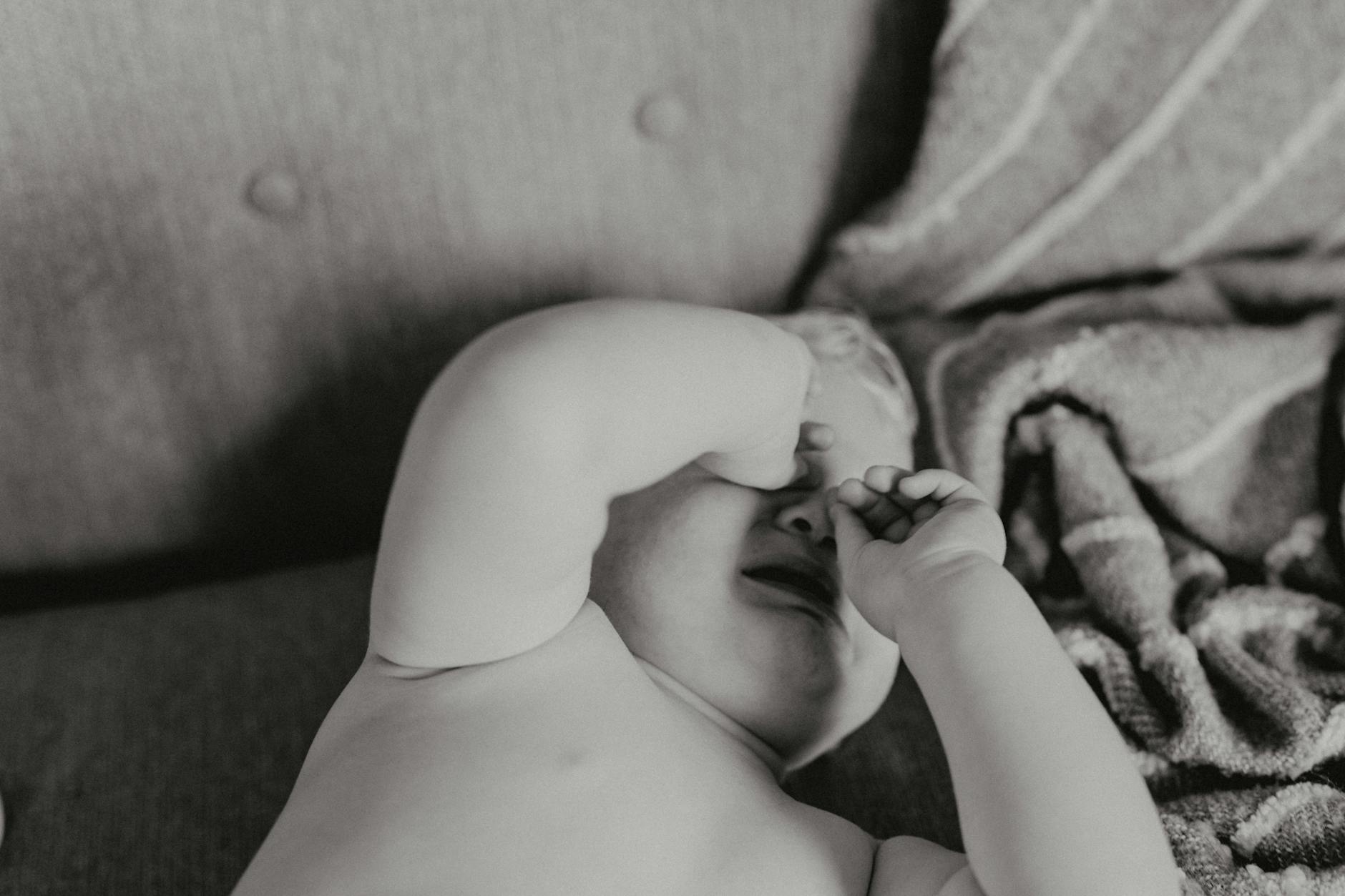 Black and white close-up of a crying toddler lying down indoors. - toddler emotional regulation