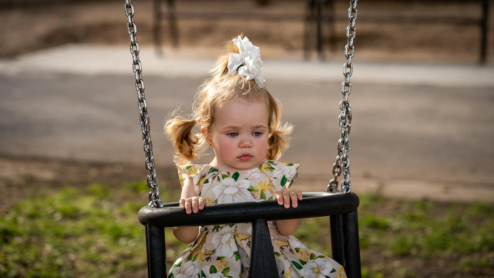 A cute toddler girl with pigtails and a floral dress on a swing in a sunny Los Angeles park. - toddler emotional regulation