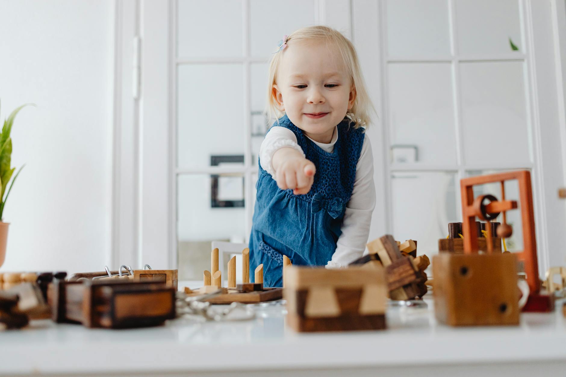 Smiling girl playing with wooden toys indoors, pointing and having fun. - toddler independence activities