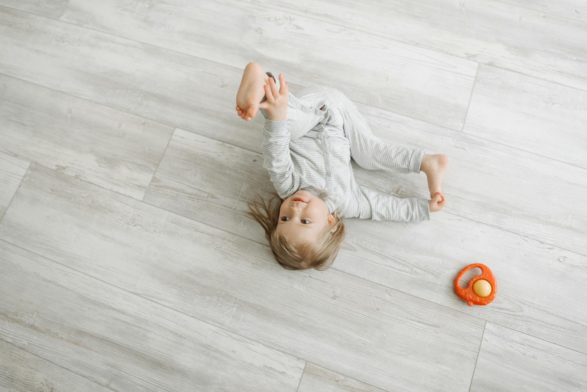 Cute child lying and playing with a toy on wooden floor, dressed warmly in pajamas. - toddler independence activities