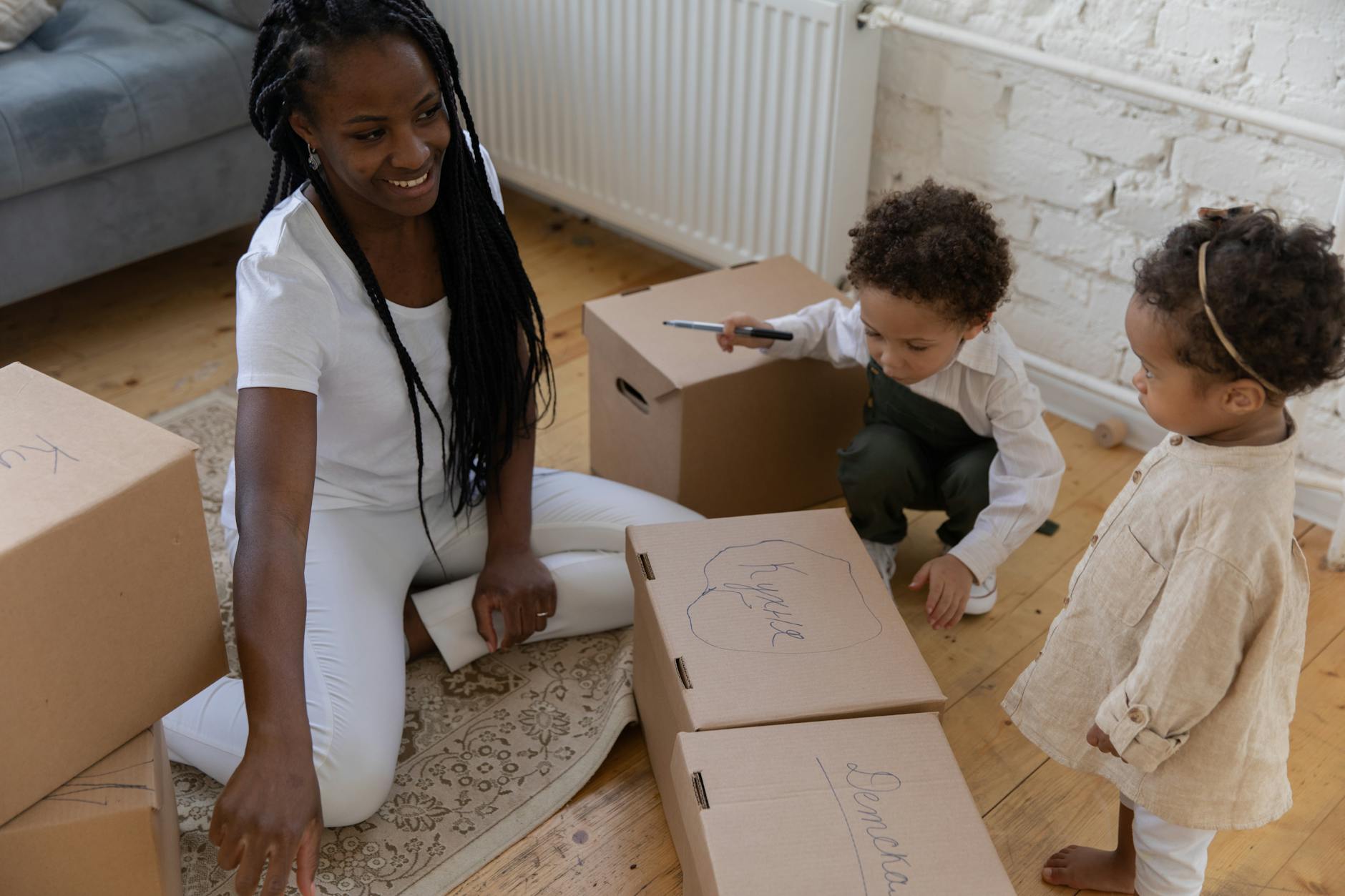 A mother and children pack cardboard boxes while sitting on the floor. - toddler independence activities