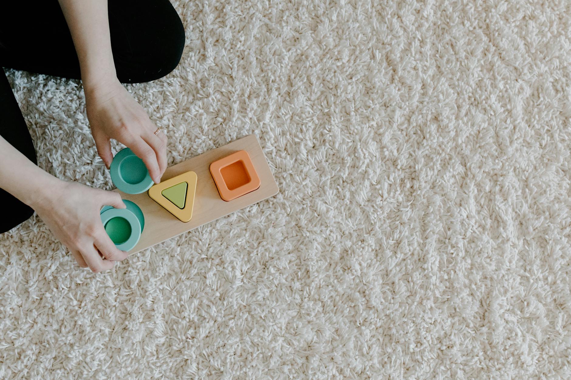 A person arranging a sustainable wooden toy on a carpet, promoting mindful and sustainable learning. - toddler independence activities