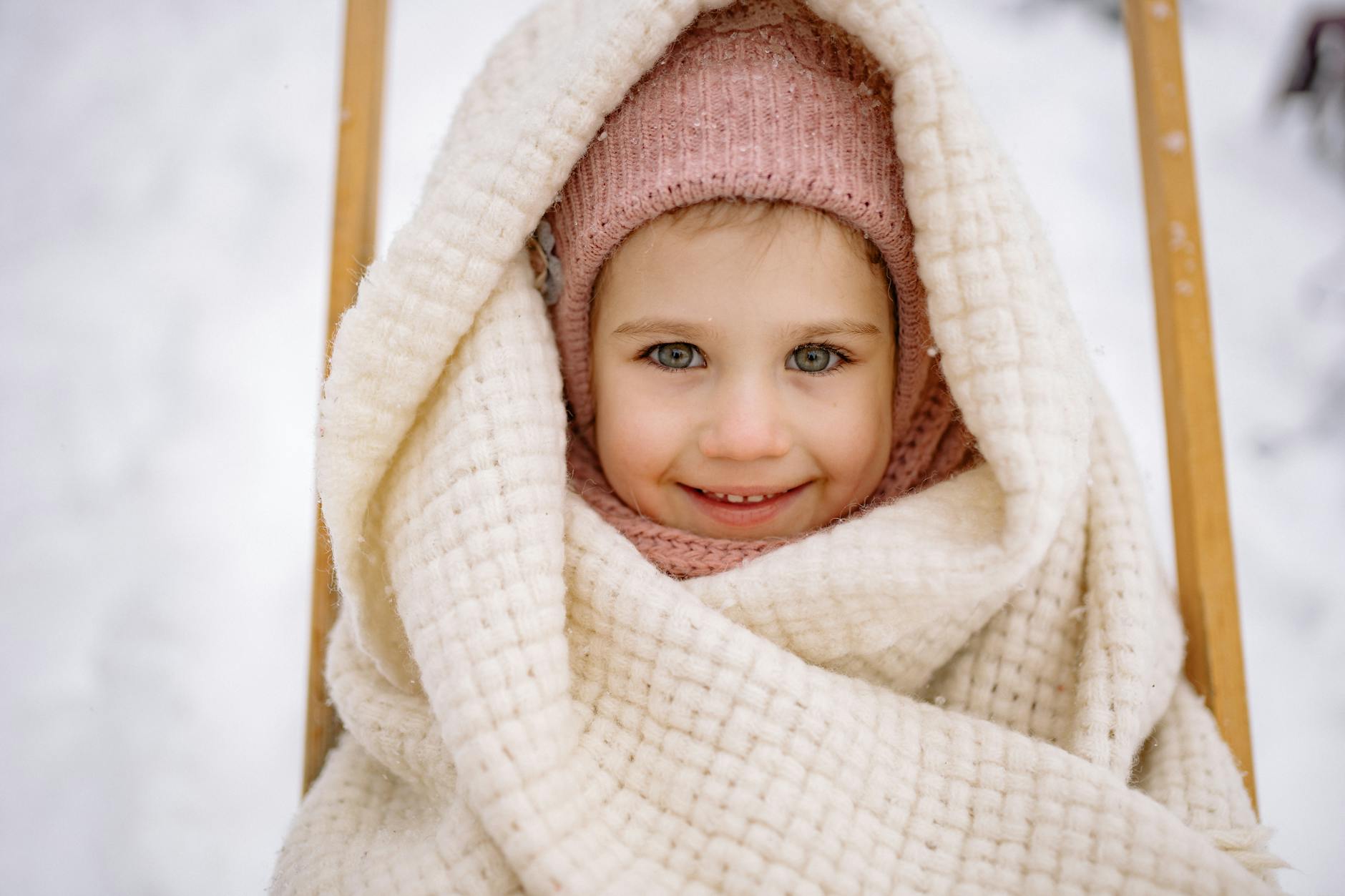 Adorable child wrapped in a warm blanket, smiling amid a snowy outdoor setting. - toddler independence winter