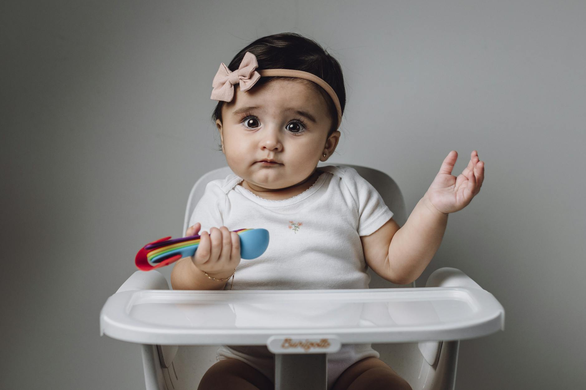 Cute baby girl sitting in a high chair with a colorful toy. - toddler language development
