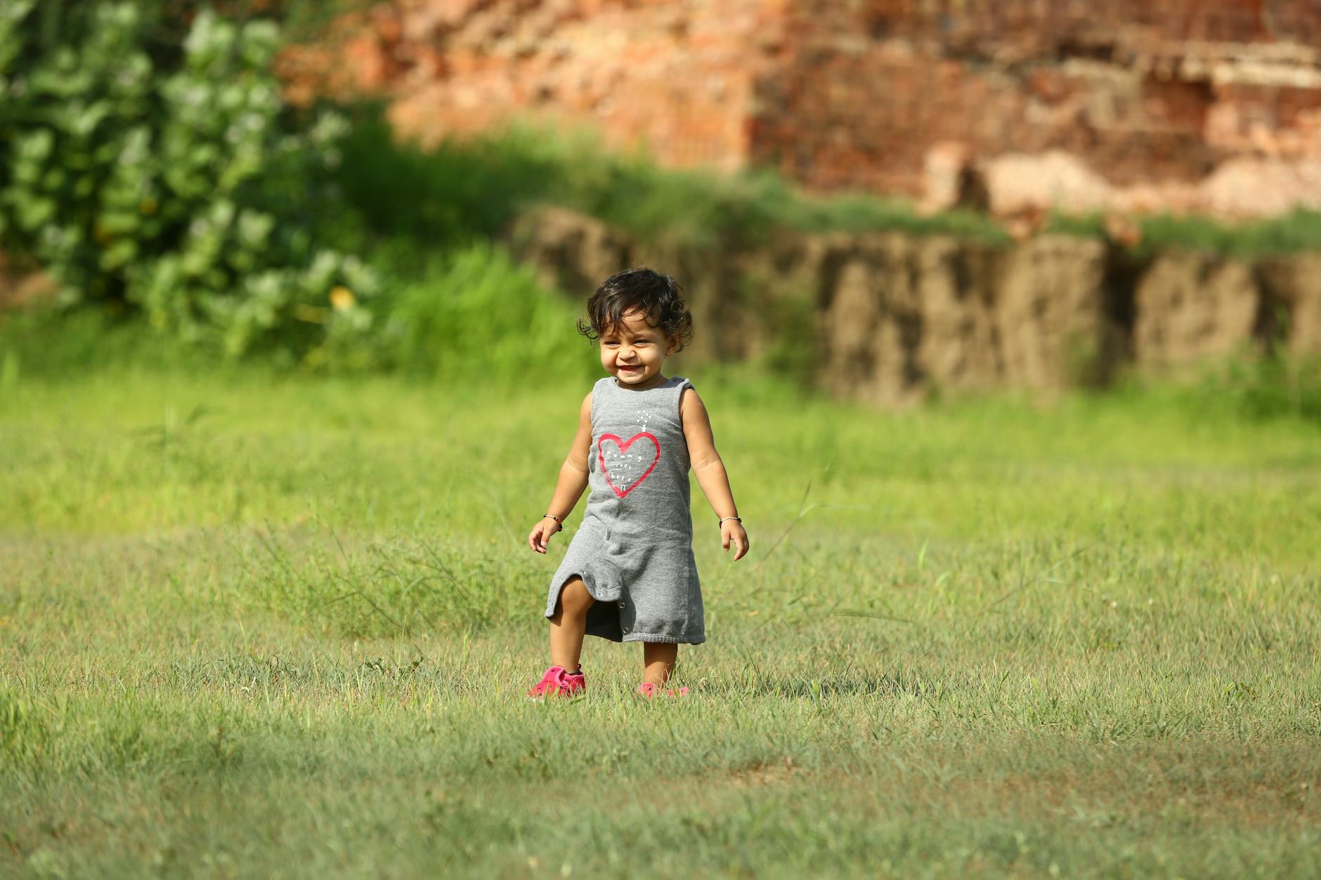 Smiling toddler in a field enjoying a sunny summer day, wearing a cute gray dress. - toddler outdoor independence