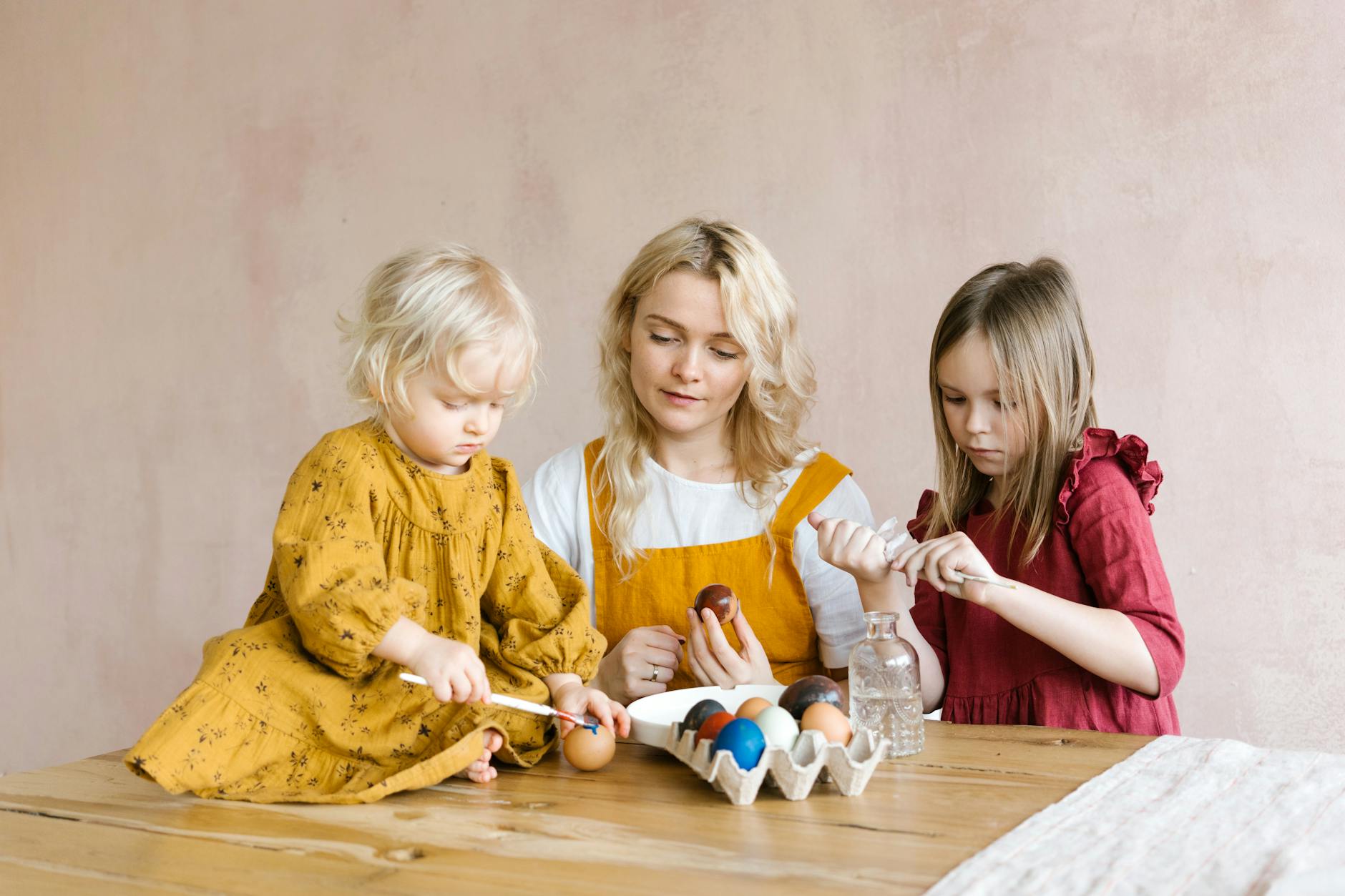 A mother and her two daughters painting colorful Easter eggs together indoors. - toddler spring activities