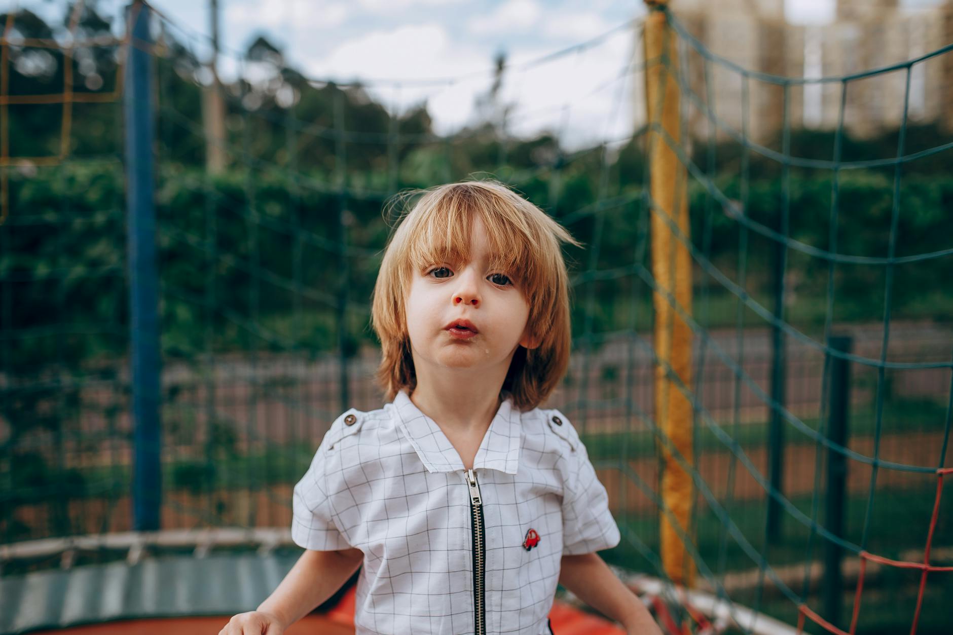 A young child enjoys playing on an outdoor playground with a netted fence in summer. - toddler spring activities
