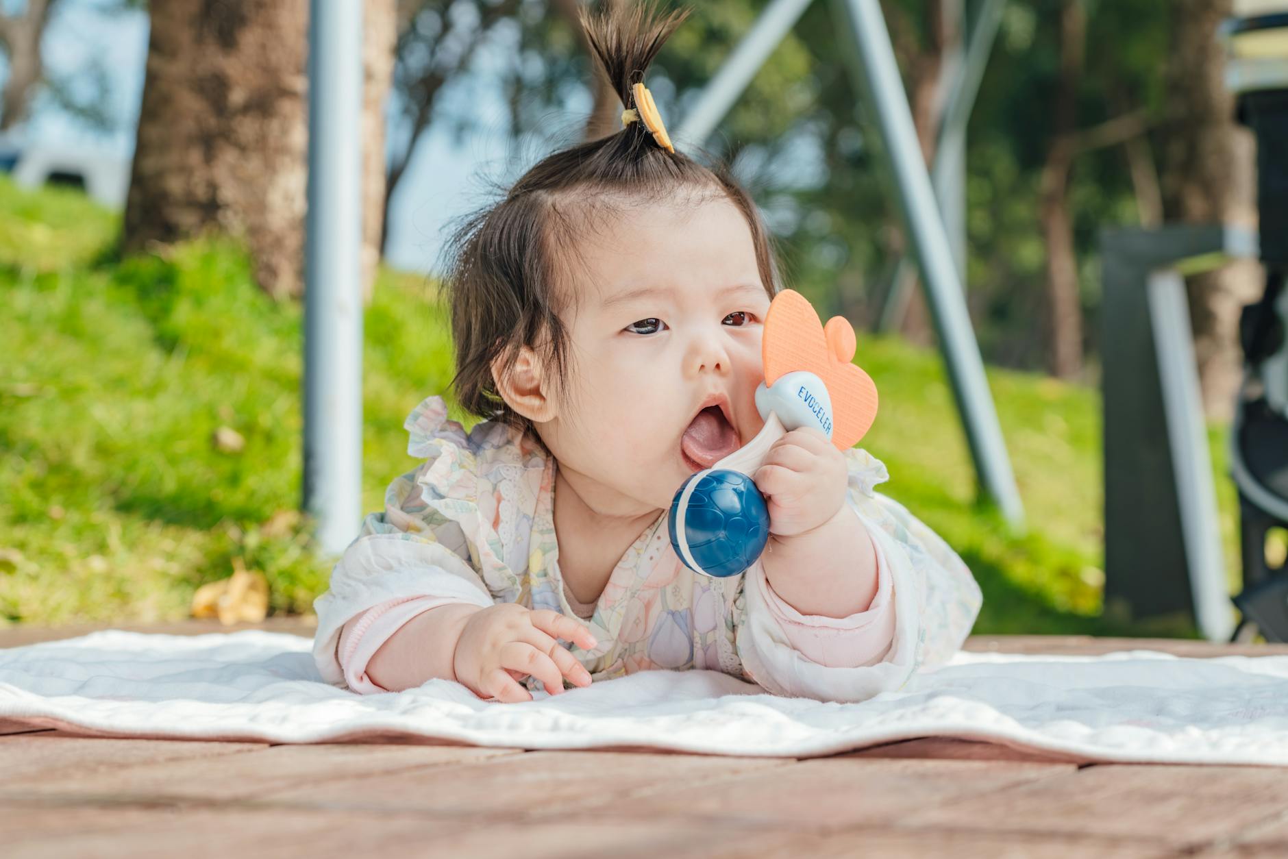 Adorable Asian baby playing with a colorful toy on a sunny day outdoors. - toddler spring activities