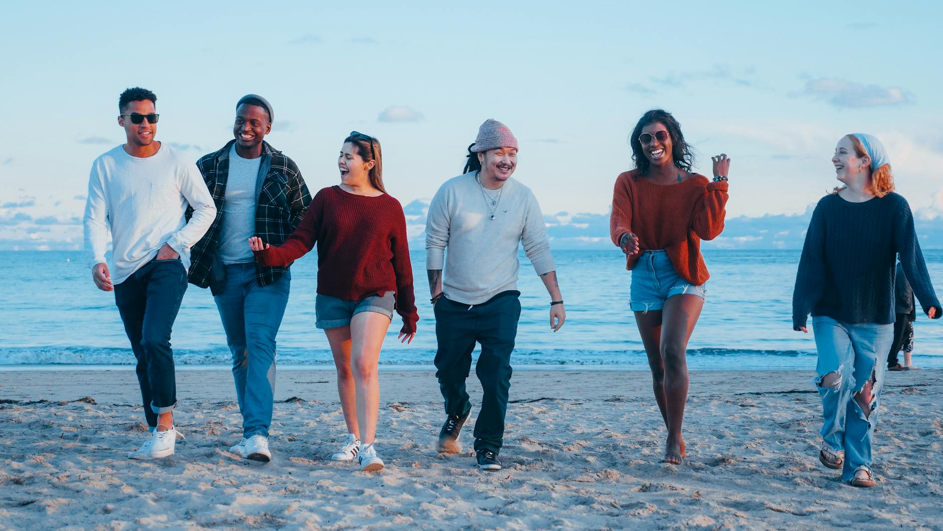 A diverse group of friends happily walking on the beach during sunset, embracing friendship and leisure. - toddler spring break
