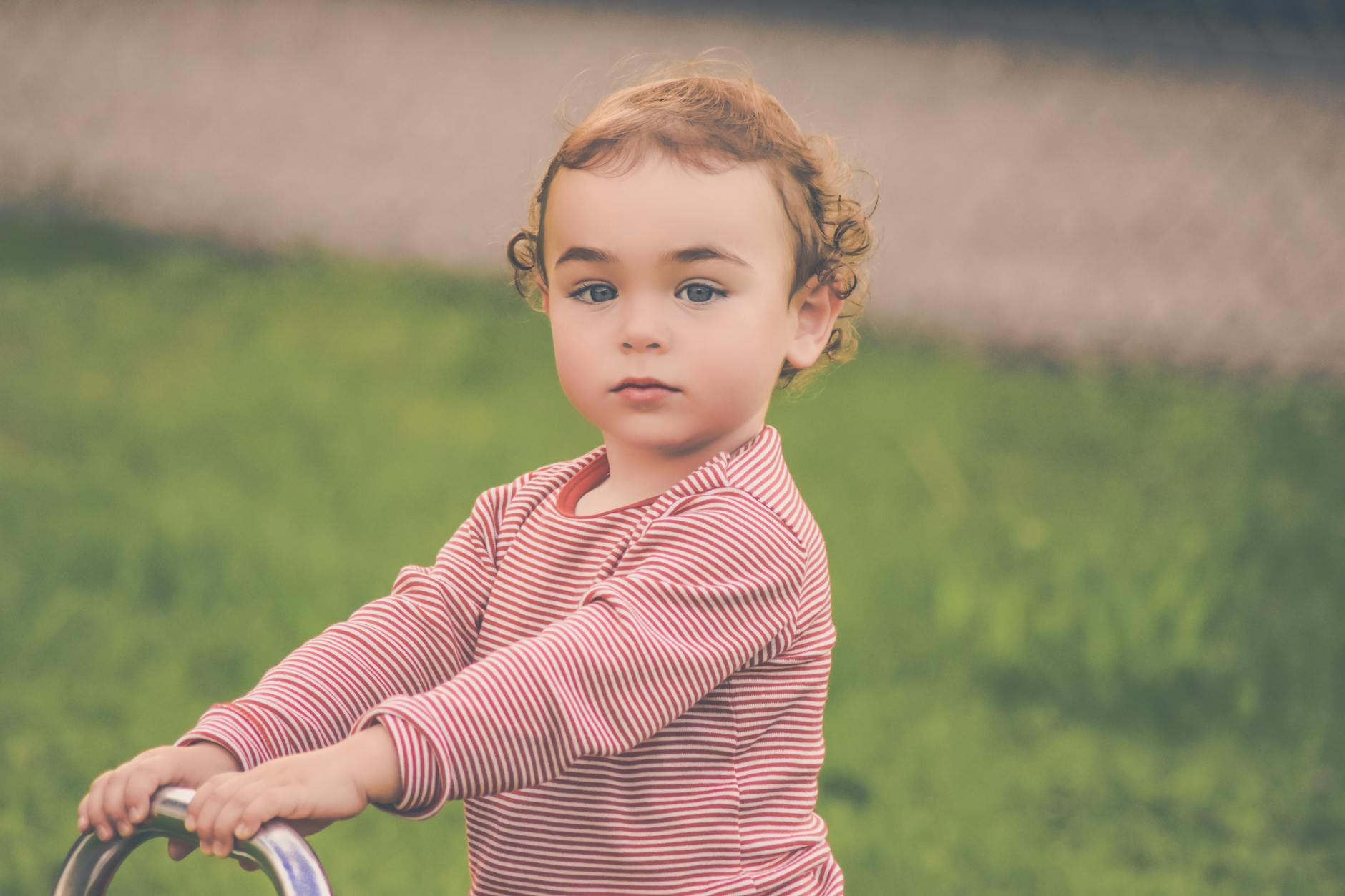Adorable young child with curly hair playing outdoors in a striped shirt, enjoying a sunny day. - toddler spring energy