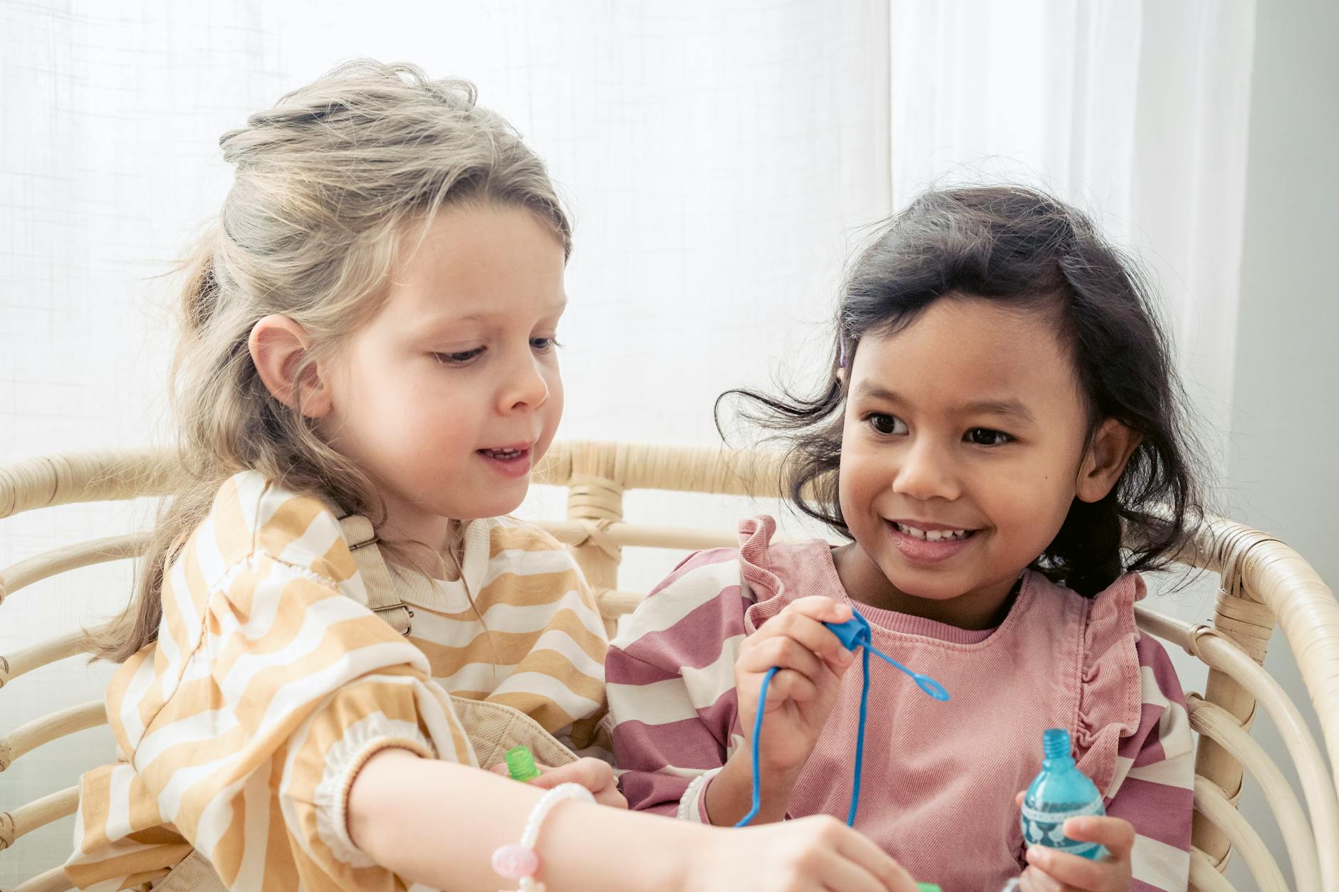 Cheerful kids enjoying playtime with bubbles in a rattan chair. - toddler spring tantrums